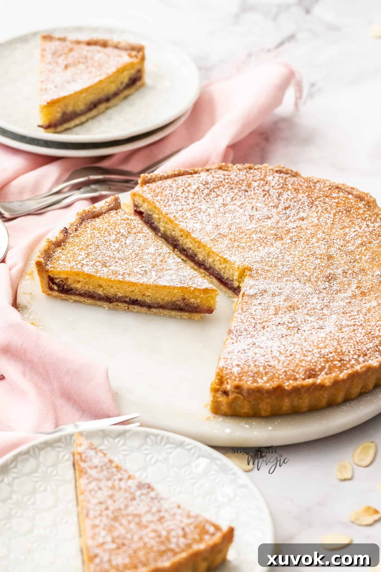 A bakewell tart, with a slice cut out, sitting on a white cake platter.
