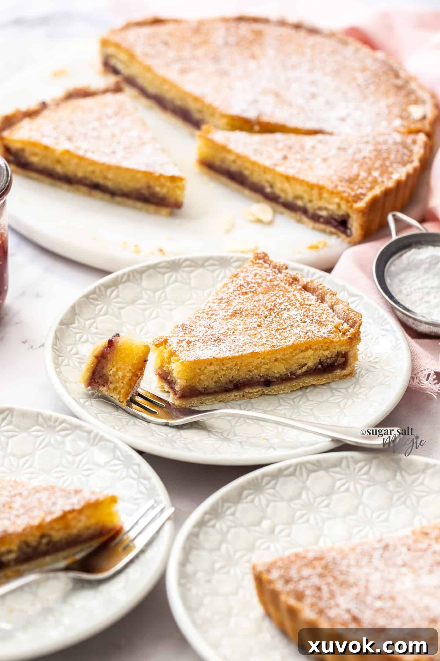 A slice of bakewell tart sitting on a white dessert plate with a forkful to the side.