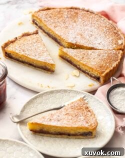 A bakewell tart cut into slices on a white marble cake platter.