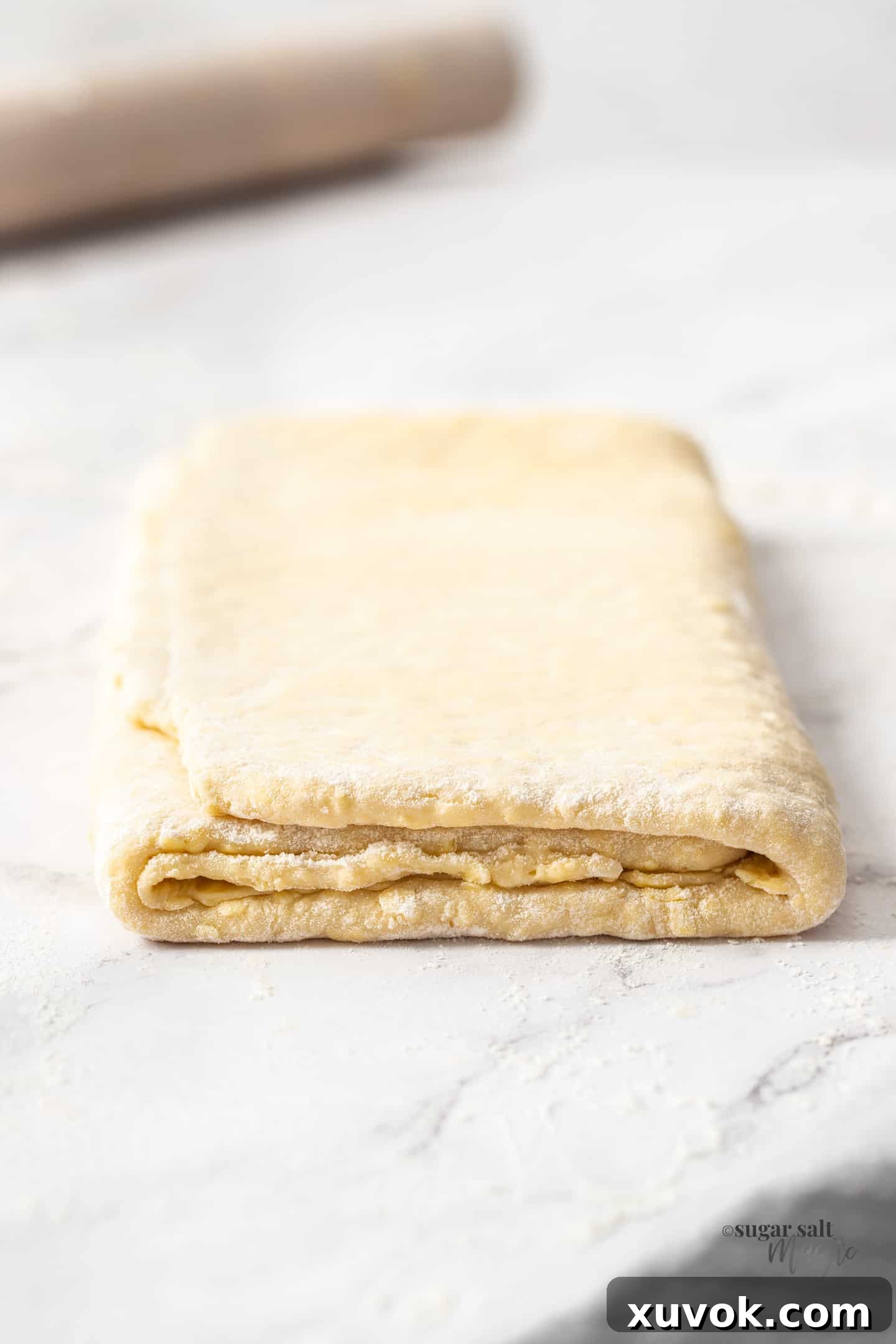 A folded sheet of danish pastry on a marble countertop, showcasing its beautiful layers.