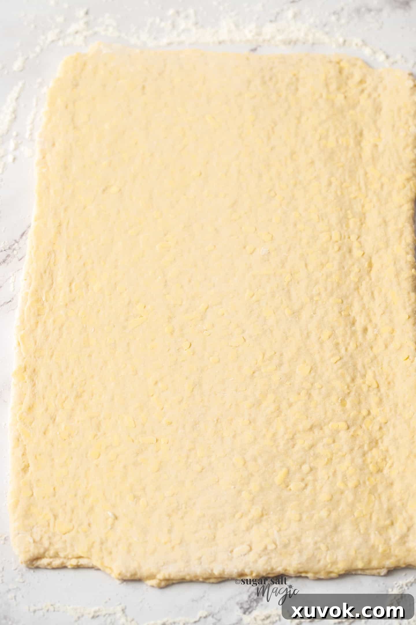 A rolled out sheet of danish pastry on a marble countertop, ready for shaping.
