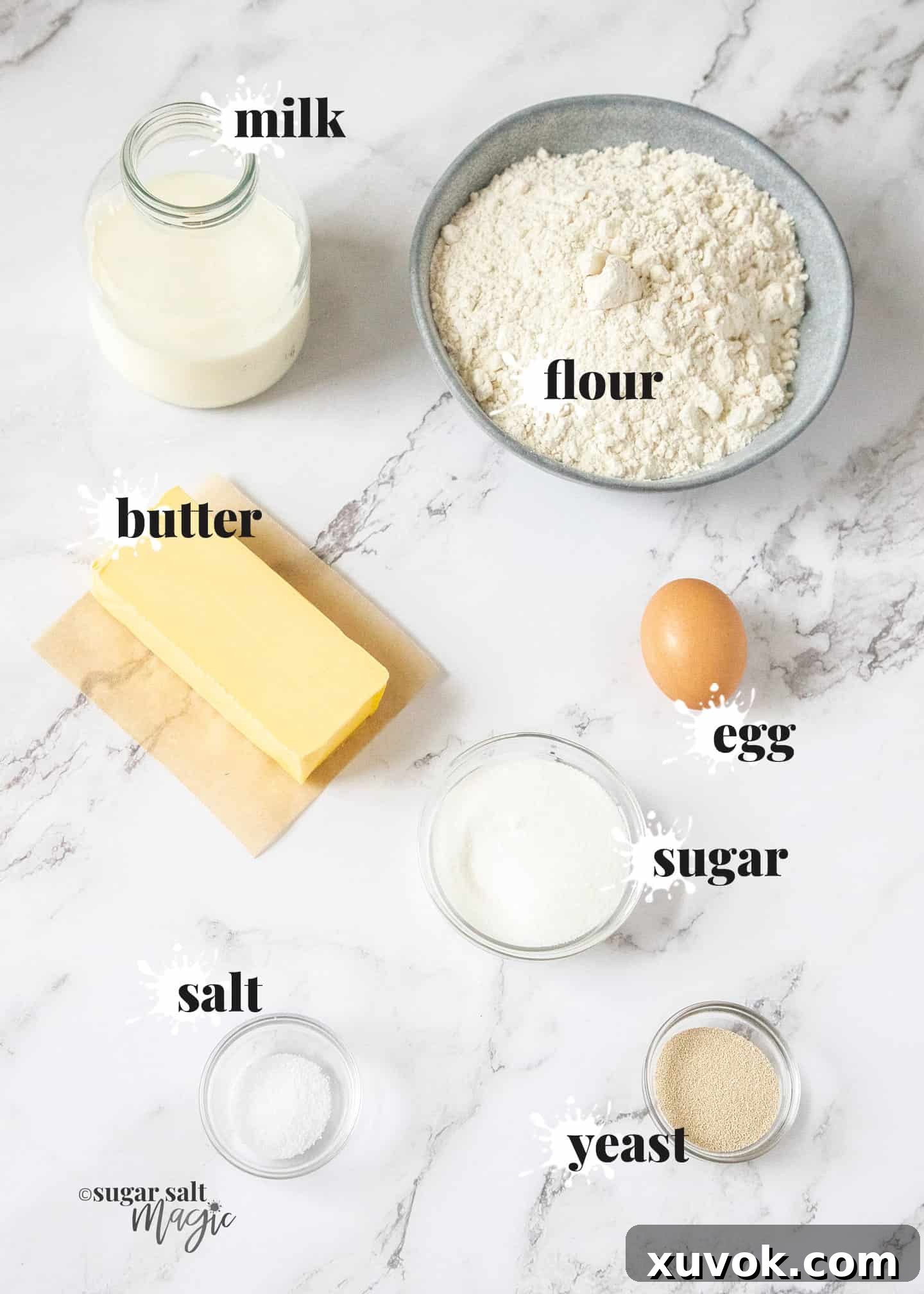 Ingredients for danish pastry dough laid out on a marble countertop: flour, butter, milk, egg, sugar, yeast, and salt.