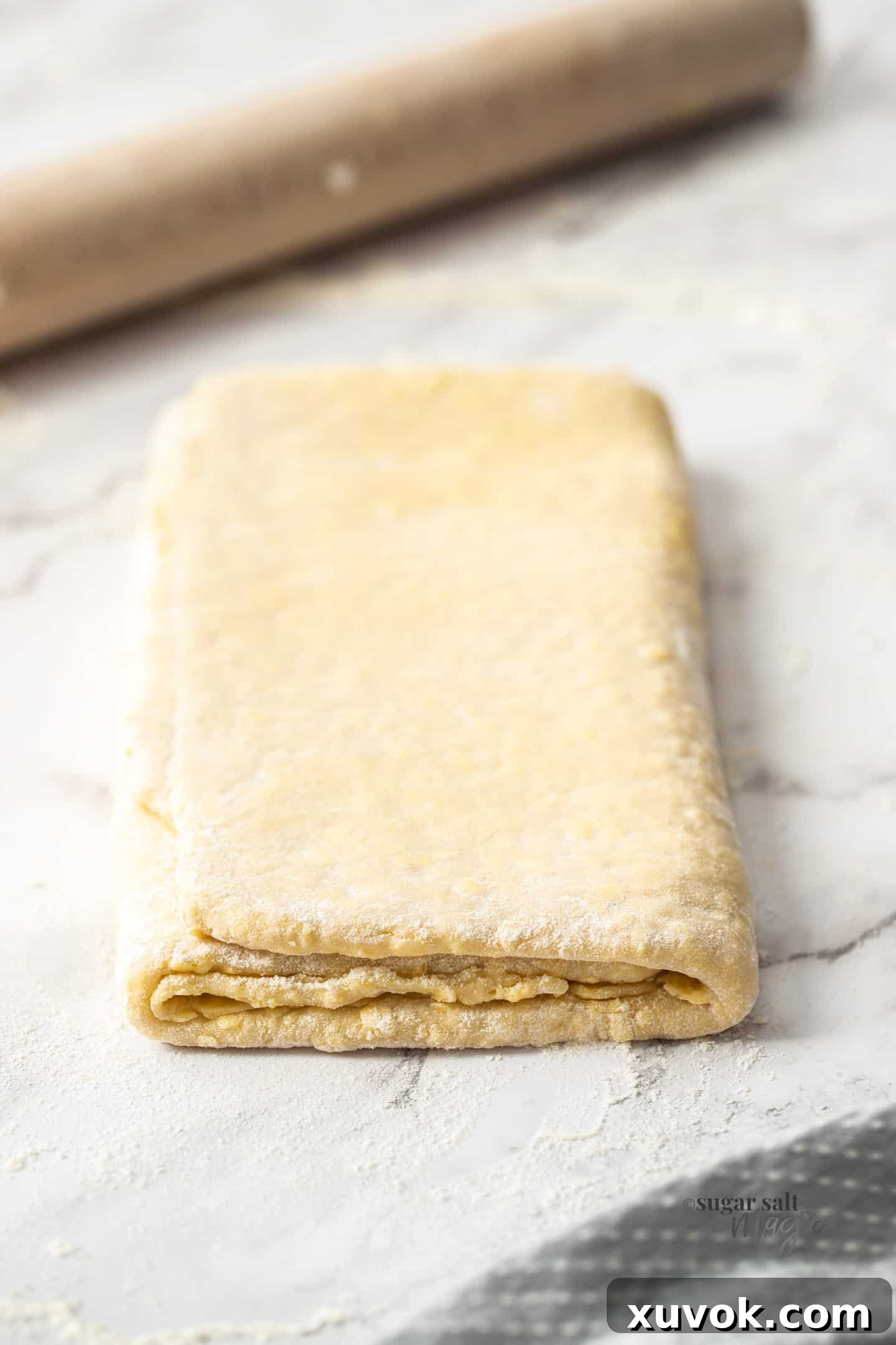 A folded sheet of Danish pastry dough on a marble countertop, showing the layered texture.