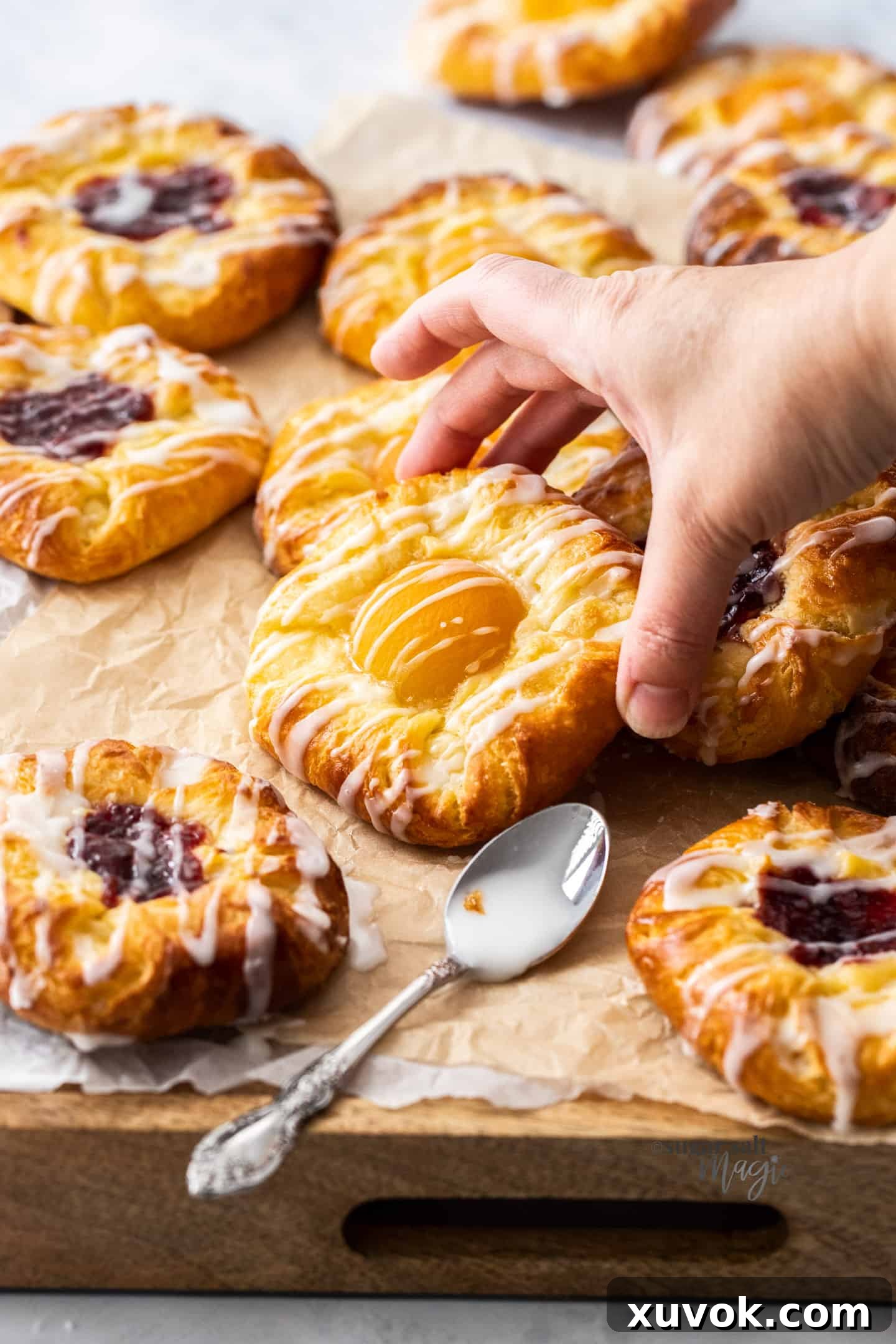 A hand reaching in to pick up a golden, flaky apricot danish from a rustic wooden board, showcasing its rich filling and perfect crust.