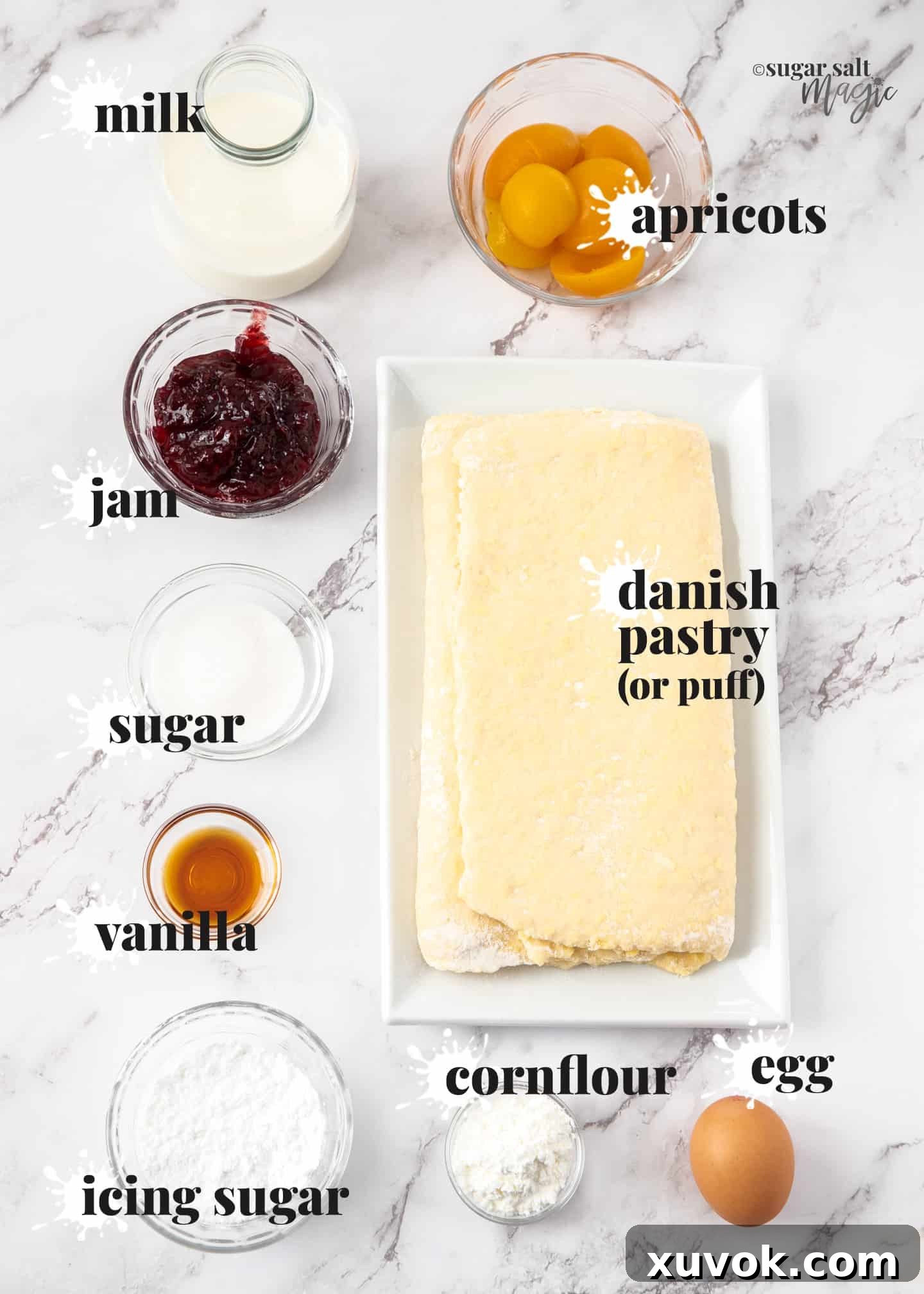 A curated display of ingredients for making custard danish pastry, including fresh apricots, various jams, and baking essentials, arranged elegantly on a marble surface.