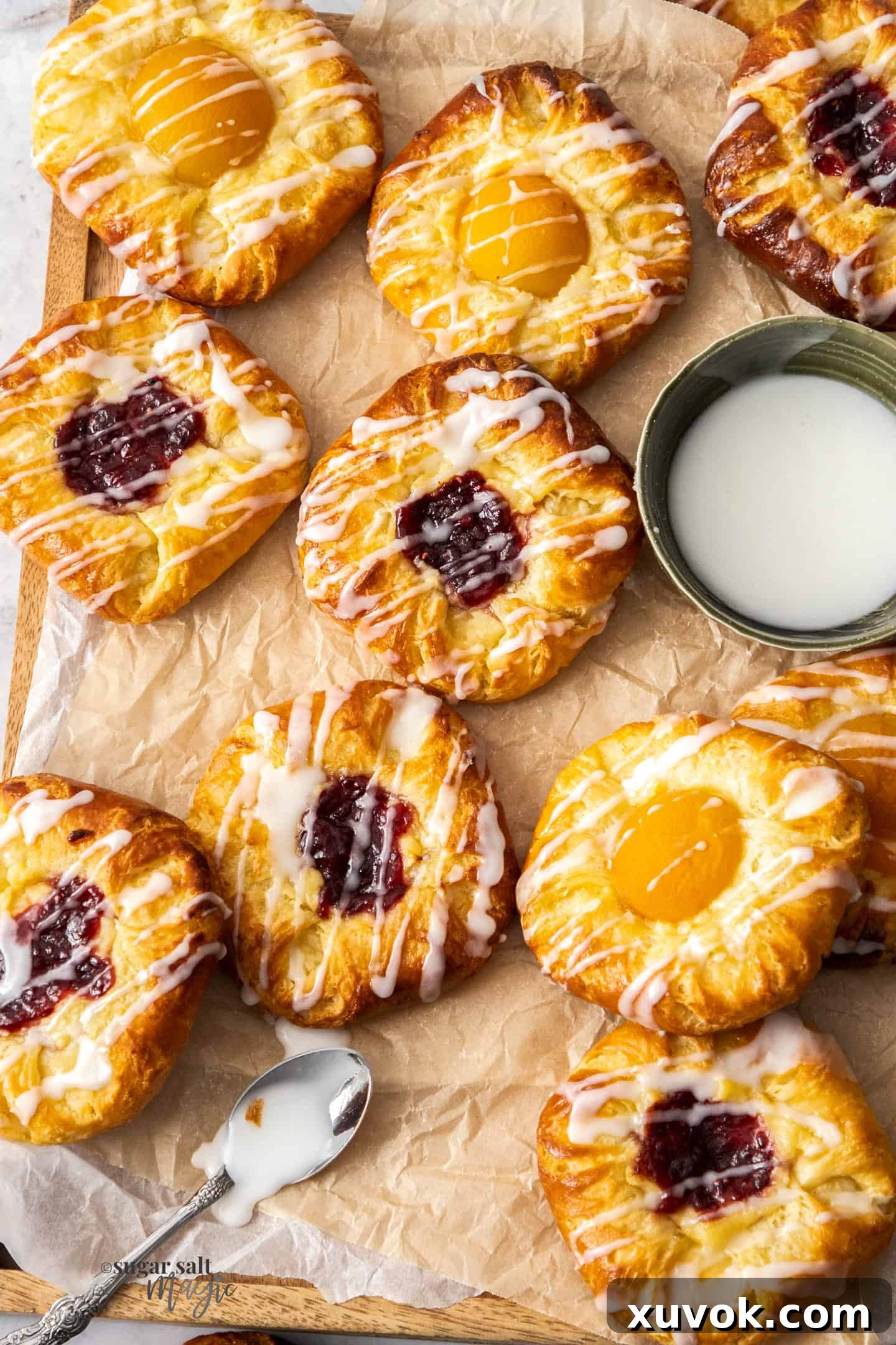 A pristine batch of freshly baked fruit custard danish pastries, glistening with glaze, arranged artfully on a sheet of baking paper.