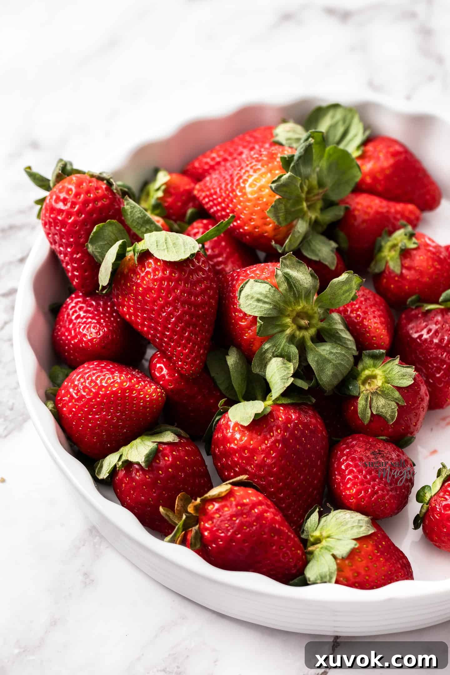 A white pie dish filled with fresh, vibrant strawberries, ready for baking.