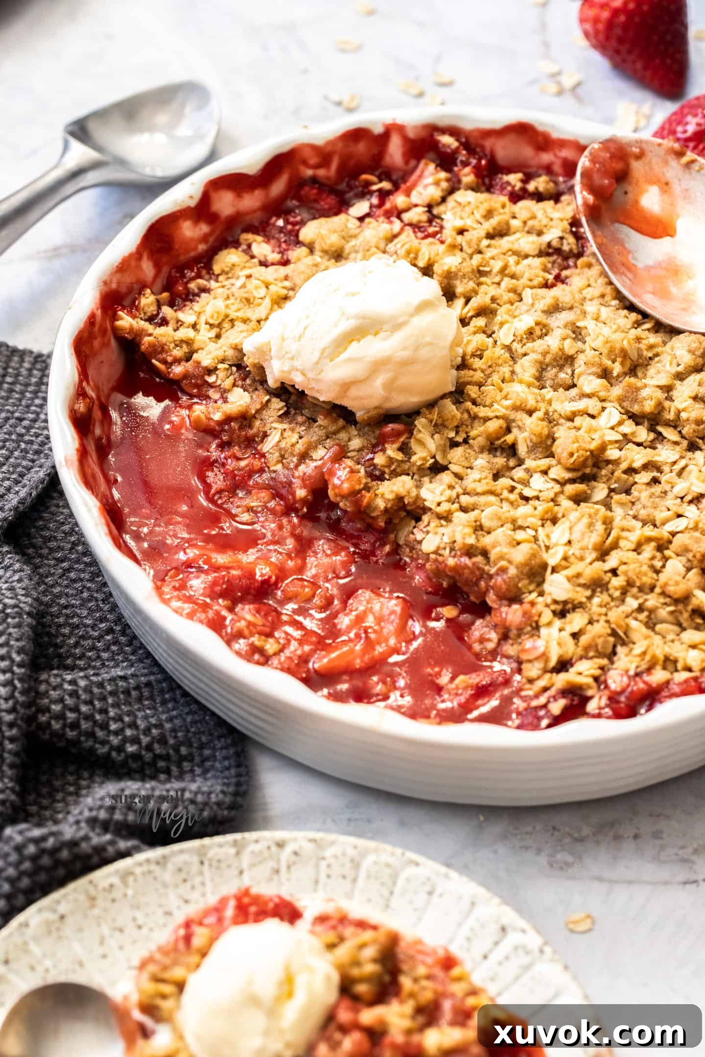 A white pie dish filled with baked strawberry crisp with a dollop of ice cream melting on top.