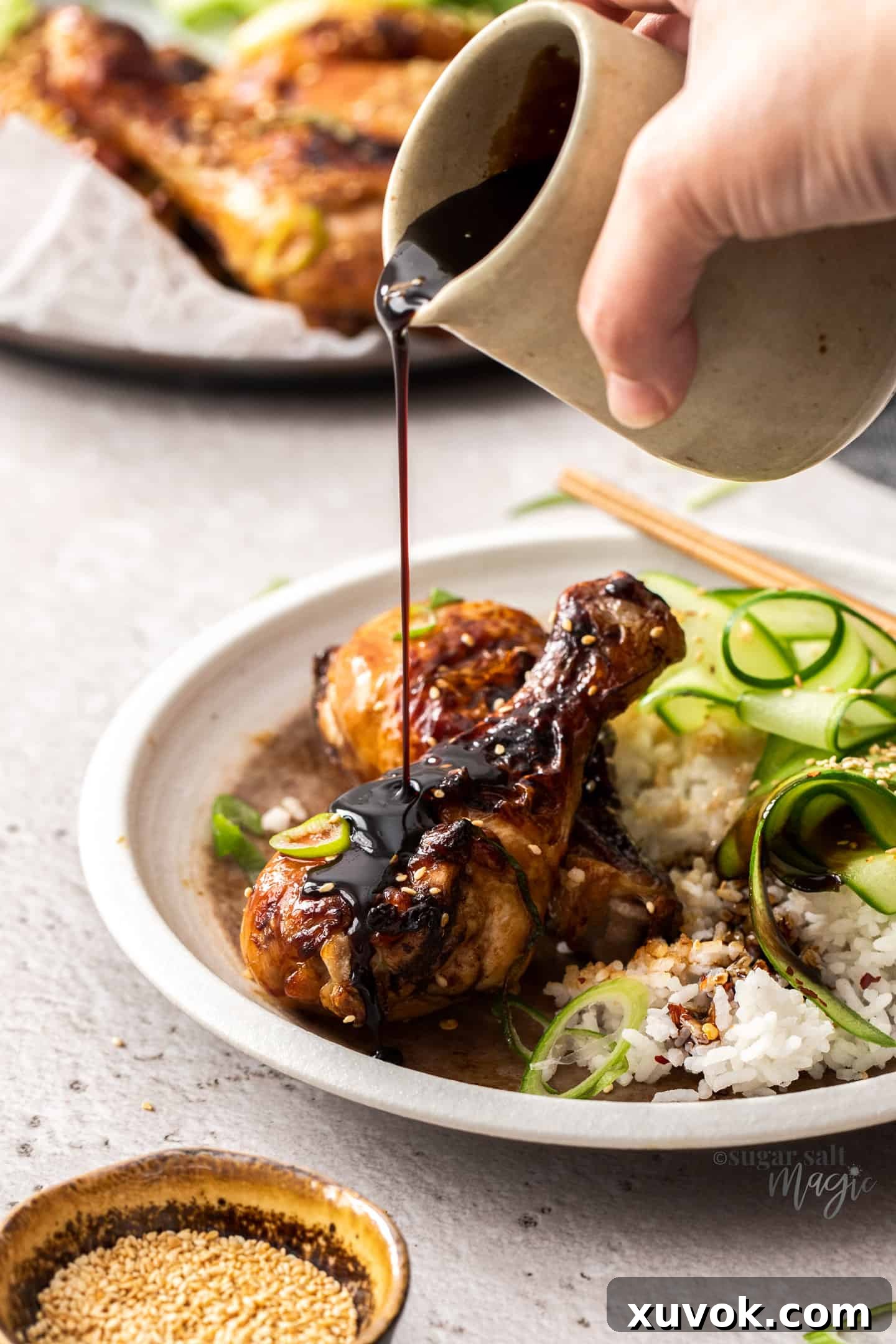 Teriyaki sauce being poured onto drumsticks on a white plate.
