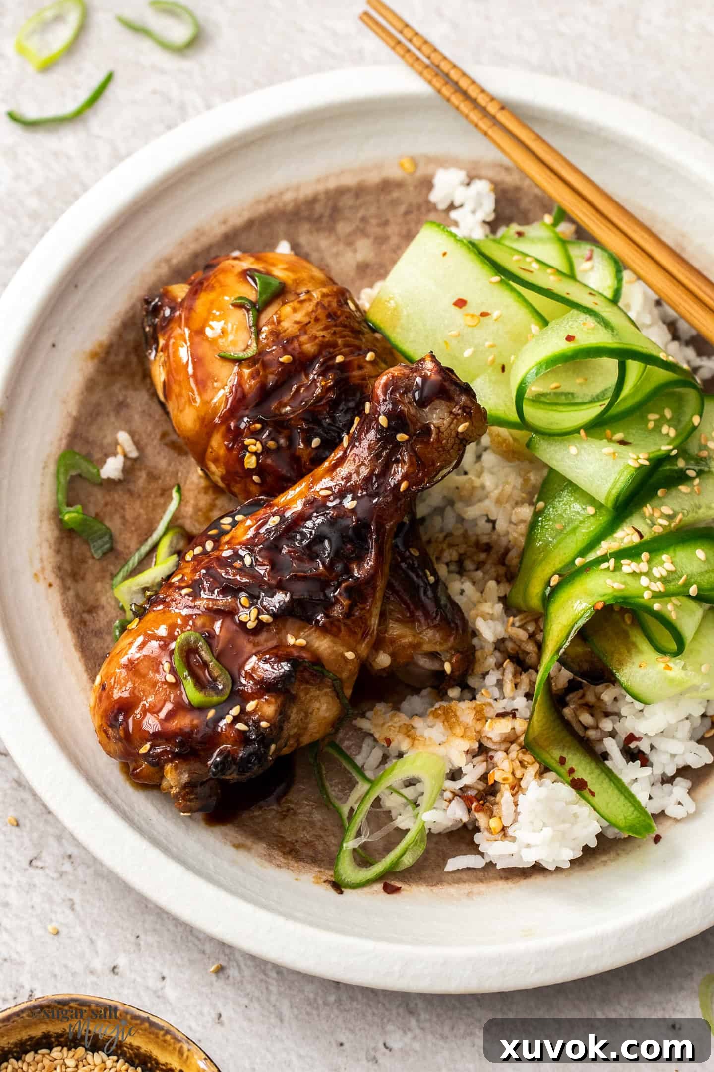 Two cooked chicken drumsticks on a white plate with rice and cucumber.