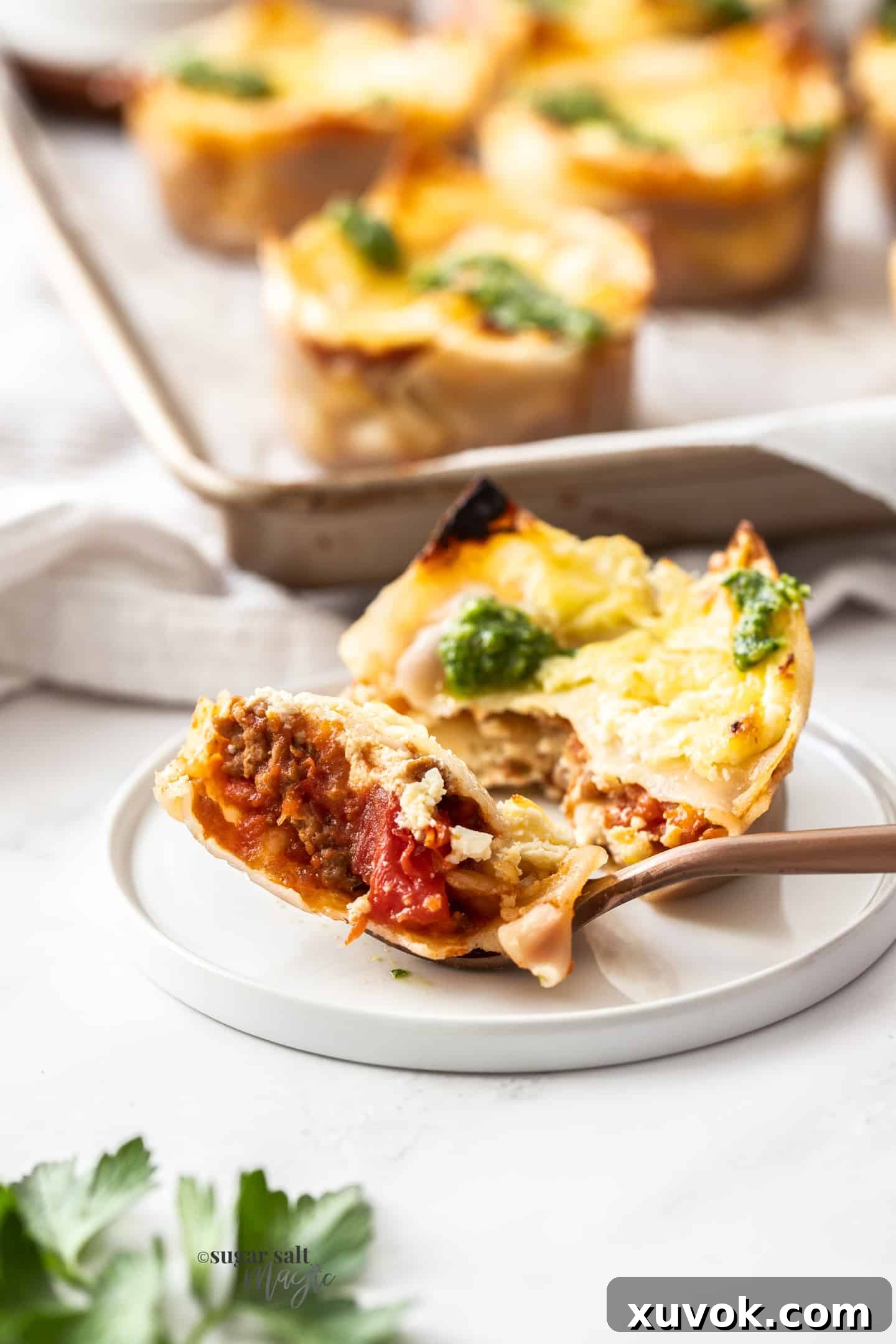 A single, perfectly baked lasagna cupcake sits on a small white plate, with a fork having removed a section, revealing the distinct layers of pasta, meat sauce, ricotta, and cheese within. The edges are visibly crisp, inviting a delightful taste.