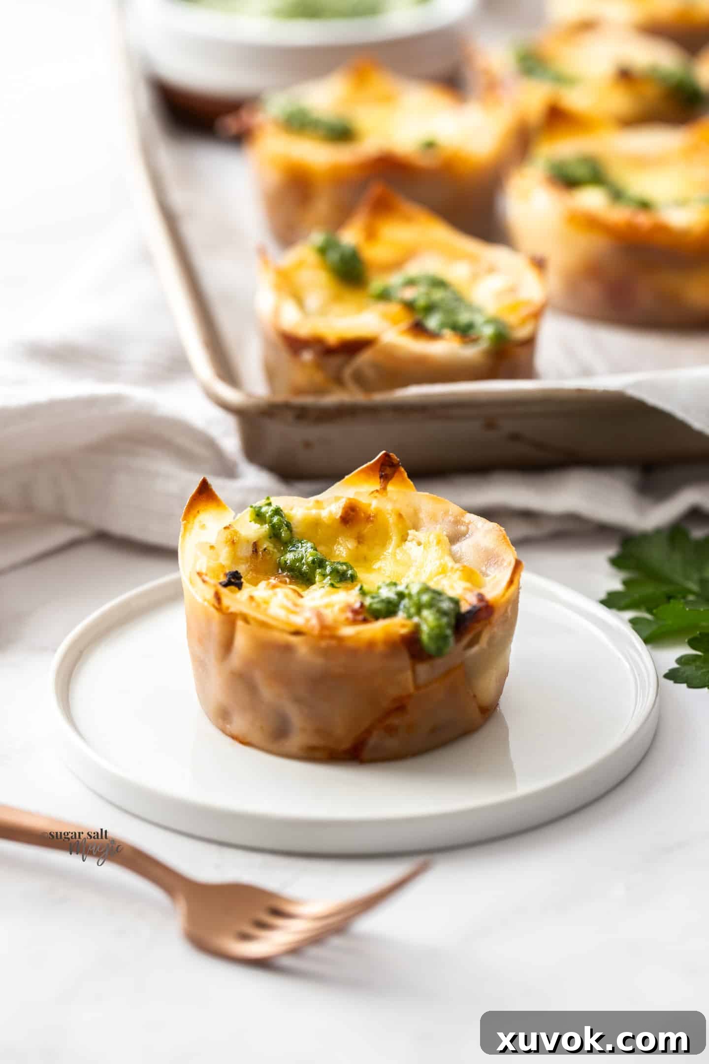 A single, golden-brown lasagna cupcake, garnished with fresh herbs, elegantly presented on a small white plate, ready to be enjoyed as a delightful appetizer.