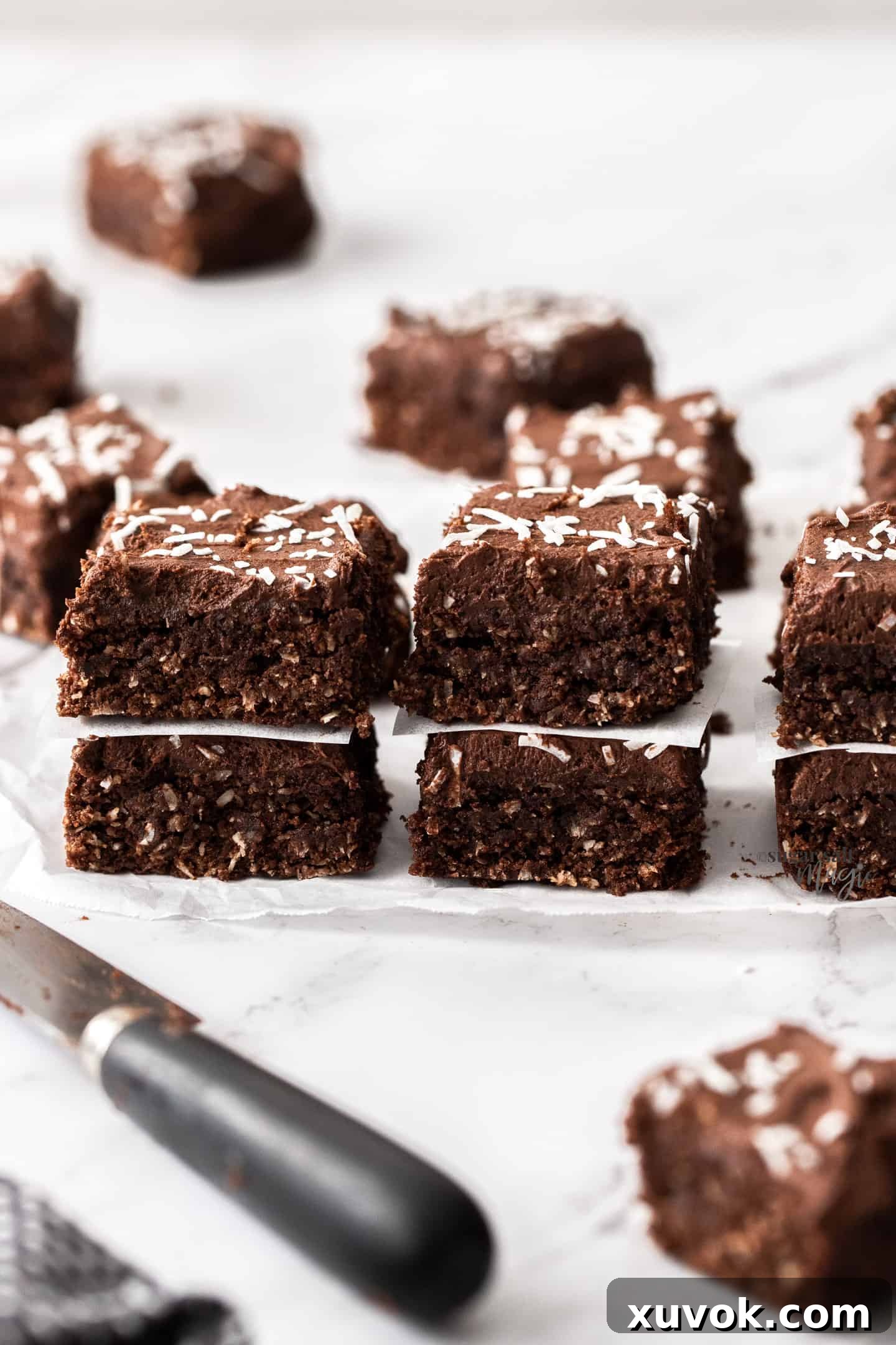 3 stacks of 2 pieces of coconut chocolate fudge slice with a knife in front, artfully arranged.