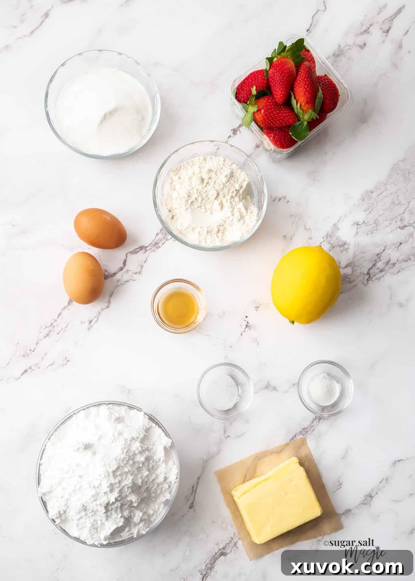 A flat lay photograph showcasing all the fresh ingredients for strawberry blondies, including strawberries, lemons, butter, eggs, sugar, and flour, arranged neatly on a white marble worktop.
