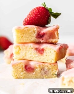 A stack of three strawberry lemon blondies, topped with a fresh strawberry, showcasing the delicious icing and texture.