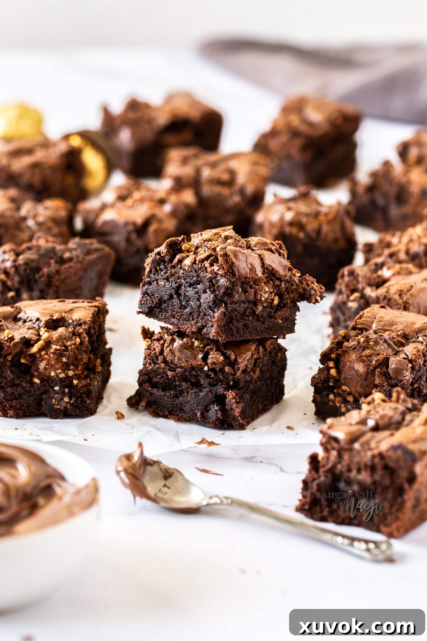 A stack of two fudgy Ferrero Rocher brownies, with more brownies scattered around, highlighting their dense texture.