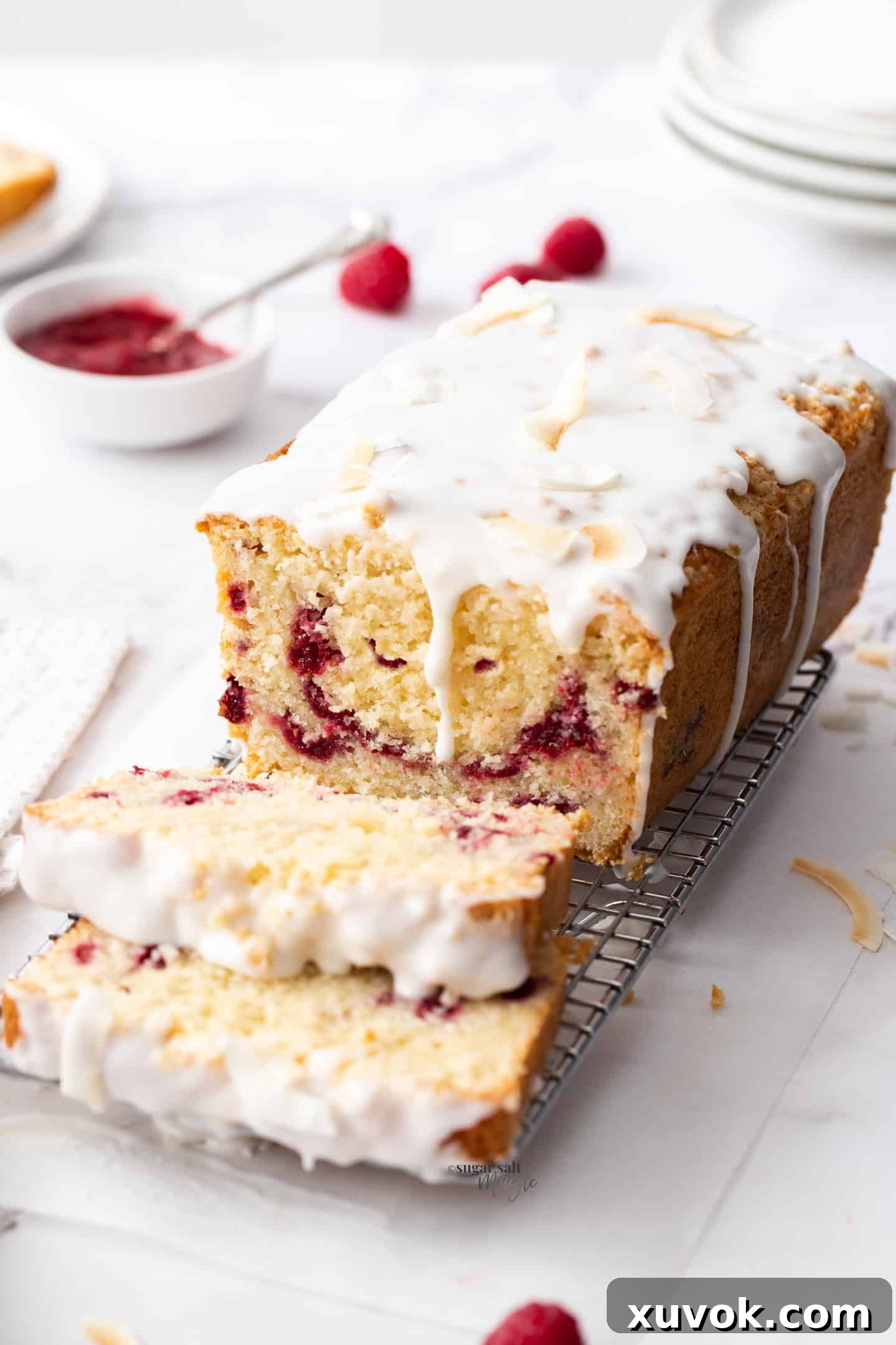 A beautifully baked coconut loaf cake, elegantly drizzled with white icing, resting on a rustic wire rack with a few fresh raspberries scattered around.