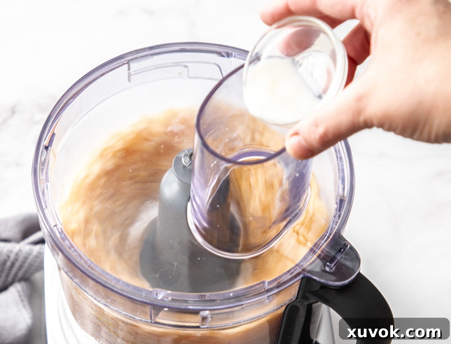 Milk being slowly poured into the food processor while it's running, to achieve the right consistency.