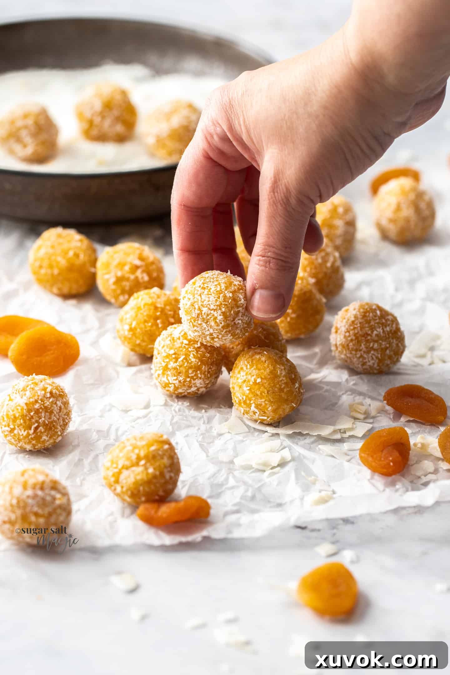 A hand reaching into a container to pick up a perfectly rolled apricot bliss ball.