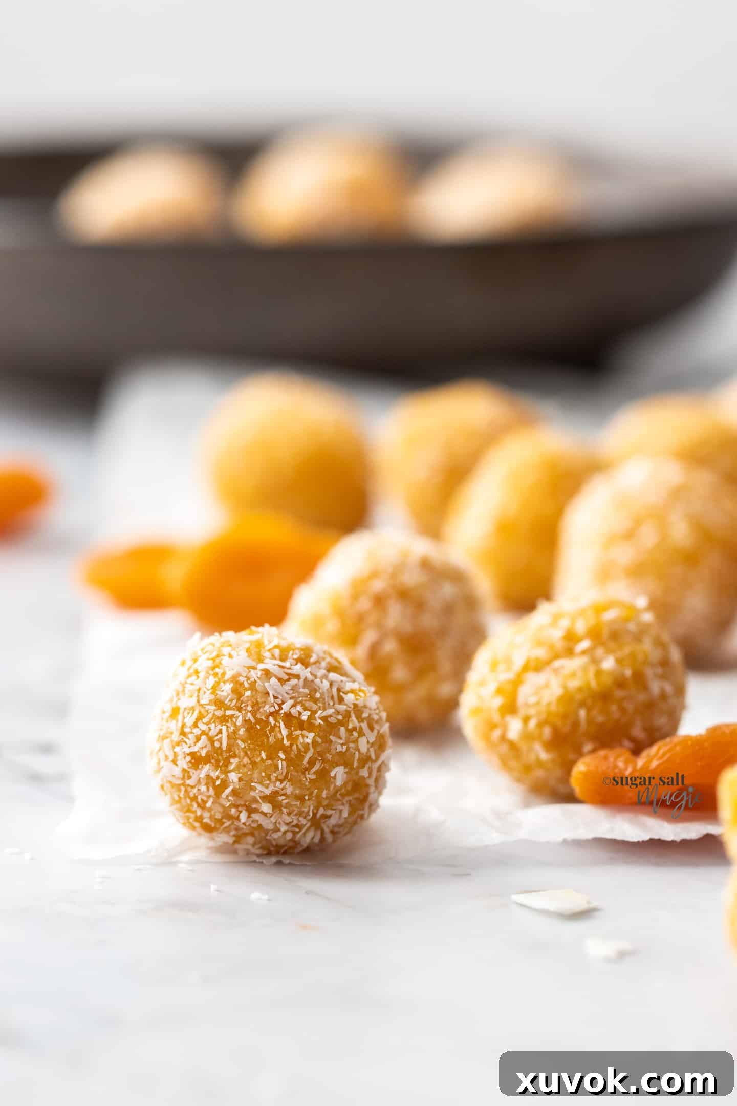 A close-up of a perfectly formed apricot bliss ball, with more blurred in the background, showcasing its delicious texture.