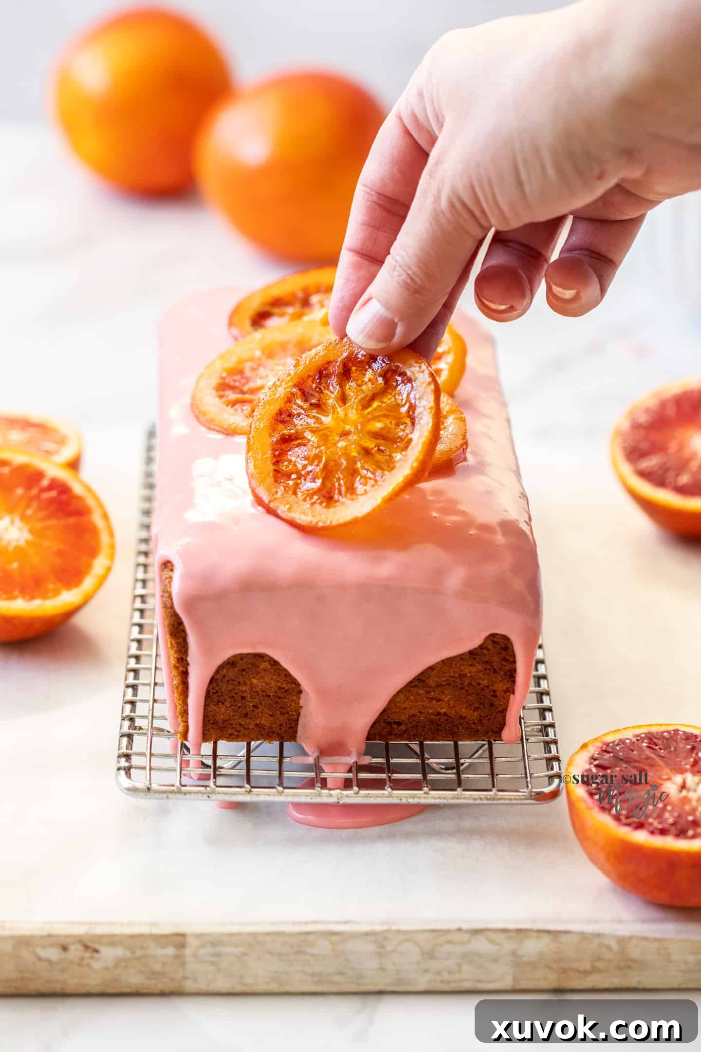 A hand placing a candied orange slice on a loaf cake