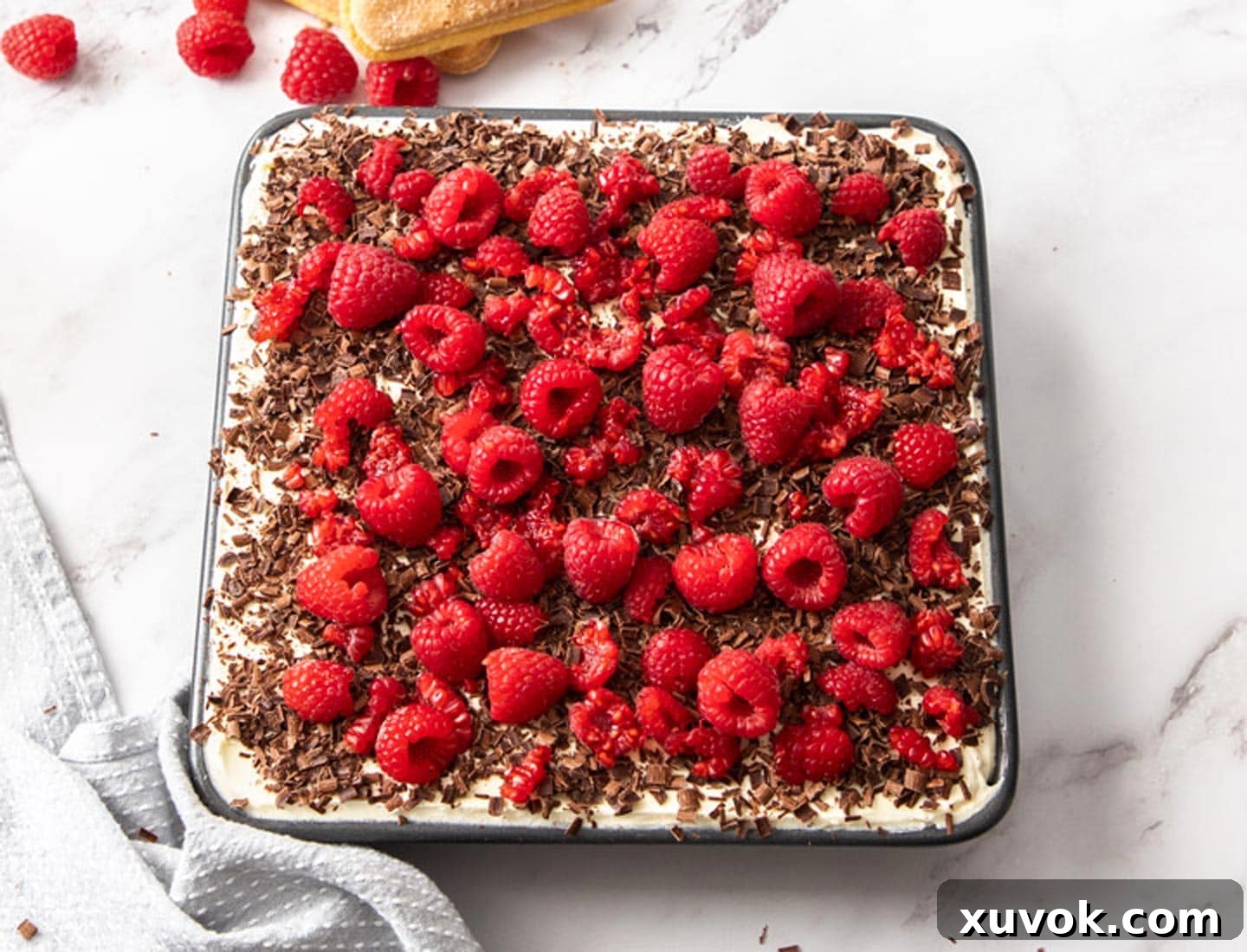 The finished raspberry tiramisu, beautifully garnished with shaved chocolate and fresh raspberries, ready to be chilled and served.