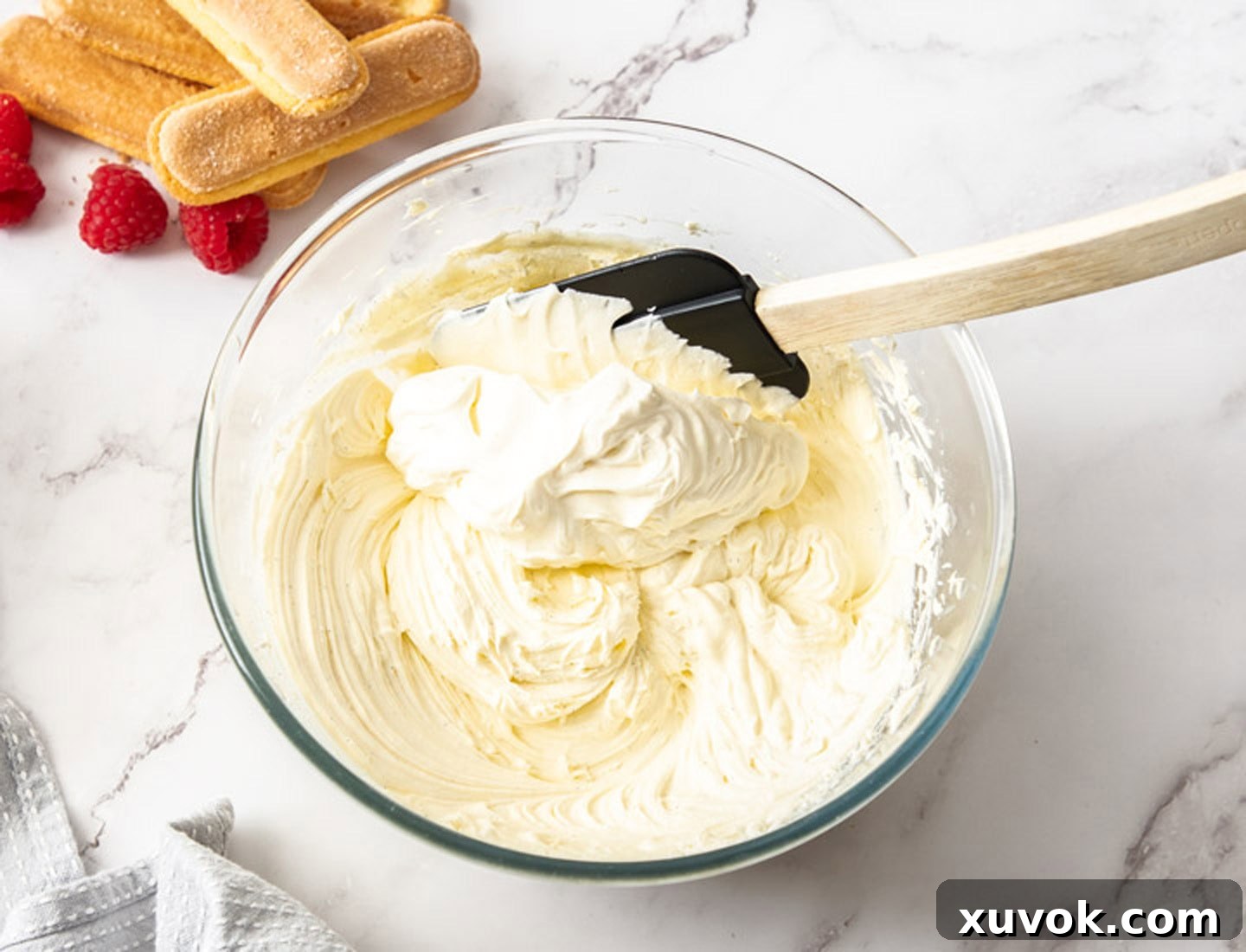 A close-up shot of whipped cream being carefully folded into a creamy mascarpone mixture in a mixing bowl, illustrating the gentle technique required.