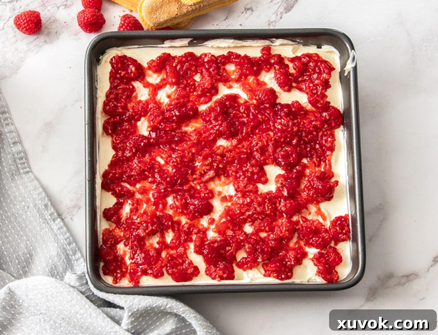 A vibrant layer of mashed raspberries generously spread on top of the creamy mascarpone mixture within the tiramisu assembly.