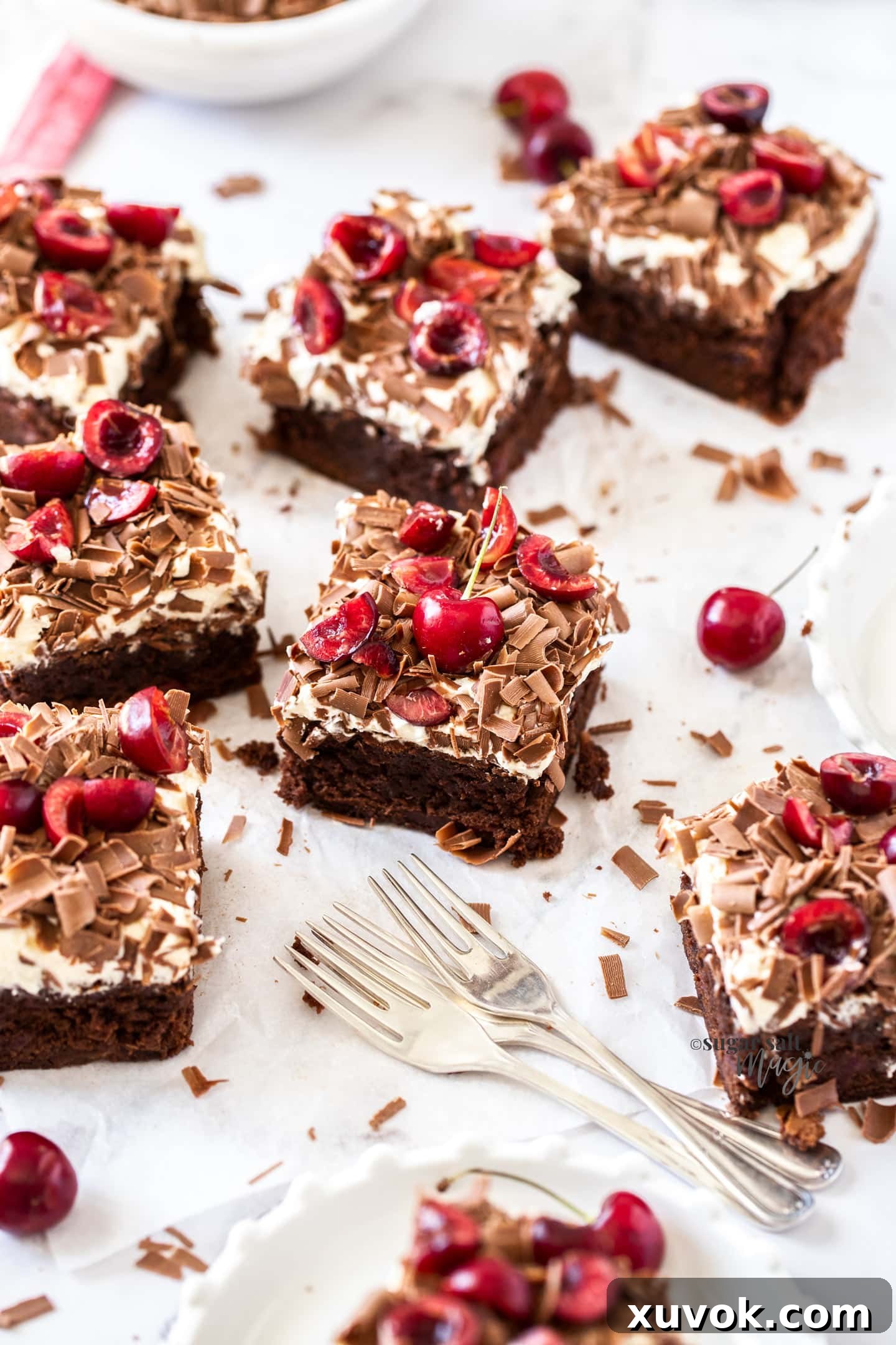 A large batch of freshly baked Black Forest Brownies, generously topped with fluffy whipped cream, bright red cherries, and delicate chocolate shavings, presented beautifully on a platter.