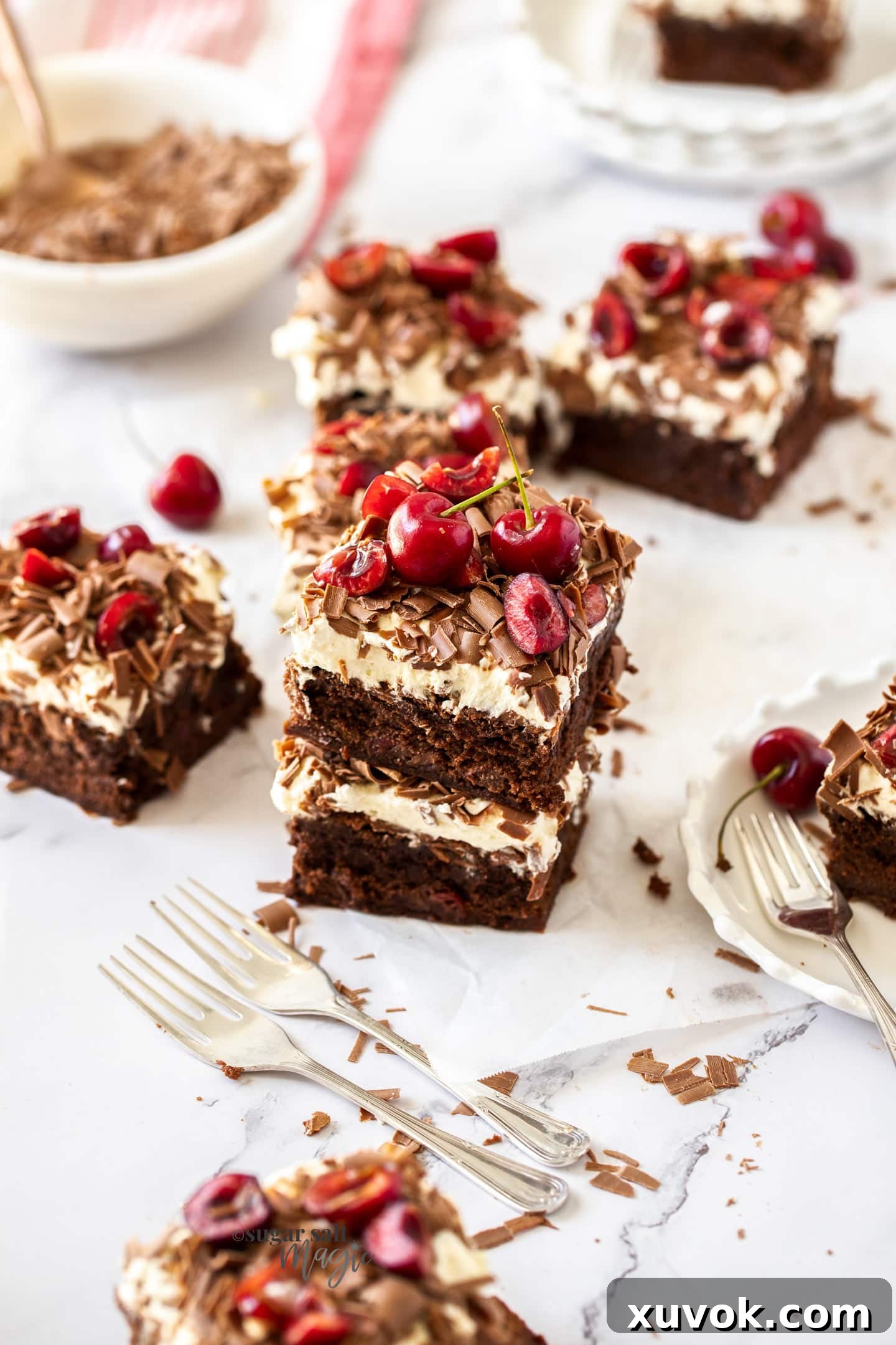 Two squares of Black Forest Brownies, stacked elegantly and topped with a generous swirl of whipped cream, vibrant fresh cherries, and delicate chocolate shavings.