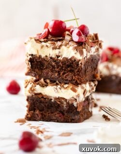 Two brownies stacked, topped with cream, cherries and chocolate