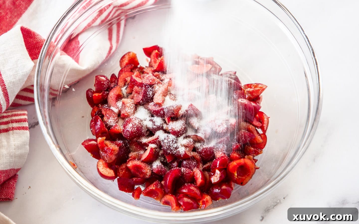 White sugar being gently sprinkled over a bowl of freshly pitted and chopped red cherries, a key step in macerating them for Black Forest Brownies.