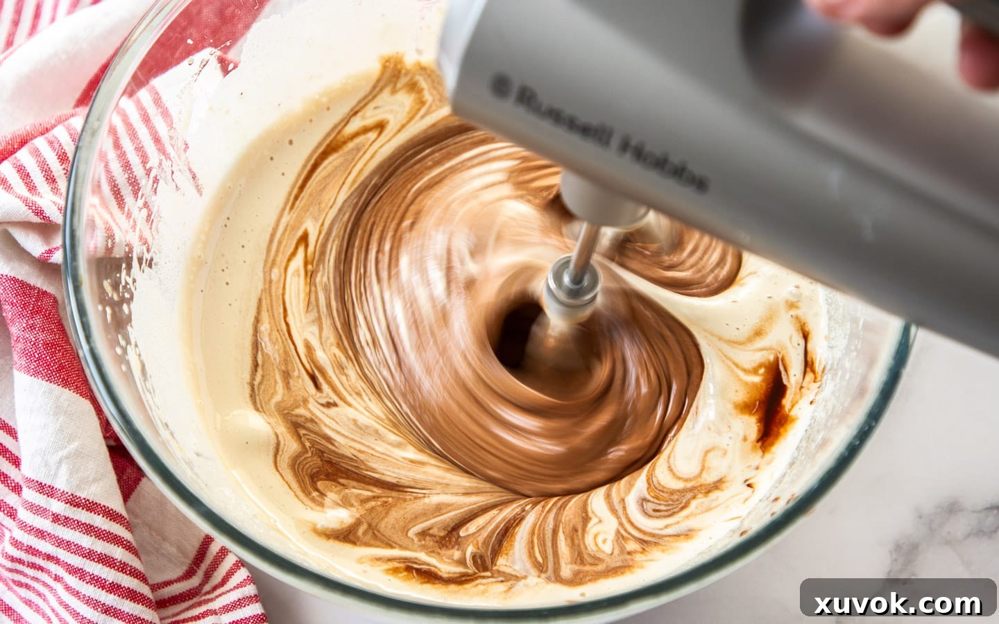 The dark, melted chocolate and butter mixture being poured into the pale, fluffy beaten eggs and sugar, ready for gentle folding.