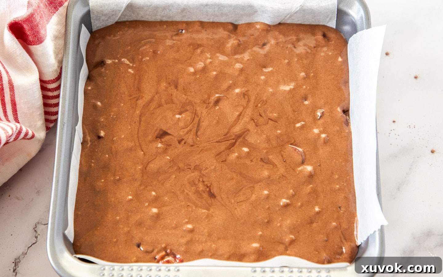 The dark, rich cherry brownie batter evenly spread in a parchment-lined square baking pan, ready for baking.