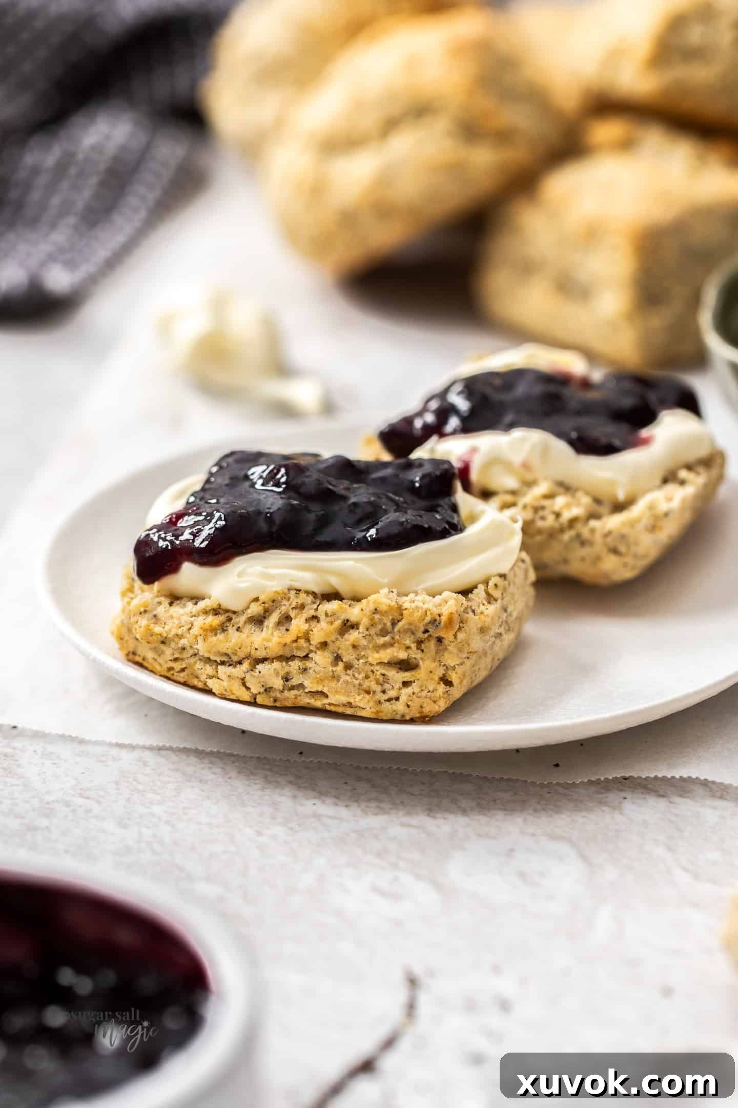 A freshly baked Earl Grey scone broken in half, revealing its flaky layers, topped with generous dollops of rich clotted cream and vibrant strawberry jam. The scene evokes a cozy tea-time moment.