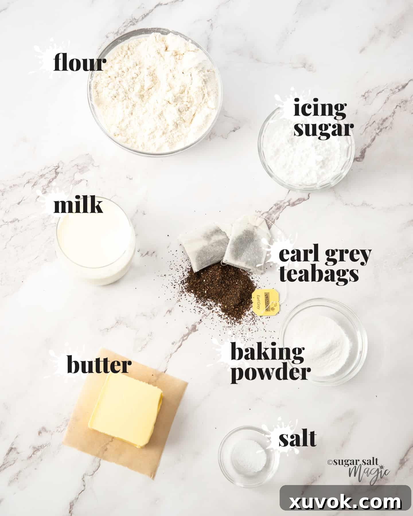 A flat lay photograph showcasing the key ingredients for Earl Grey scones laid out on a pristine marble countertop, including tea bags, flour, sugar, butter, and milk.
