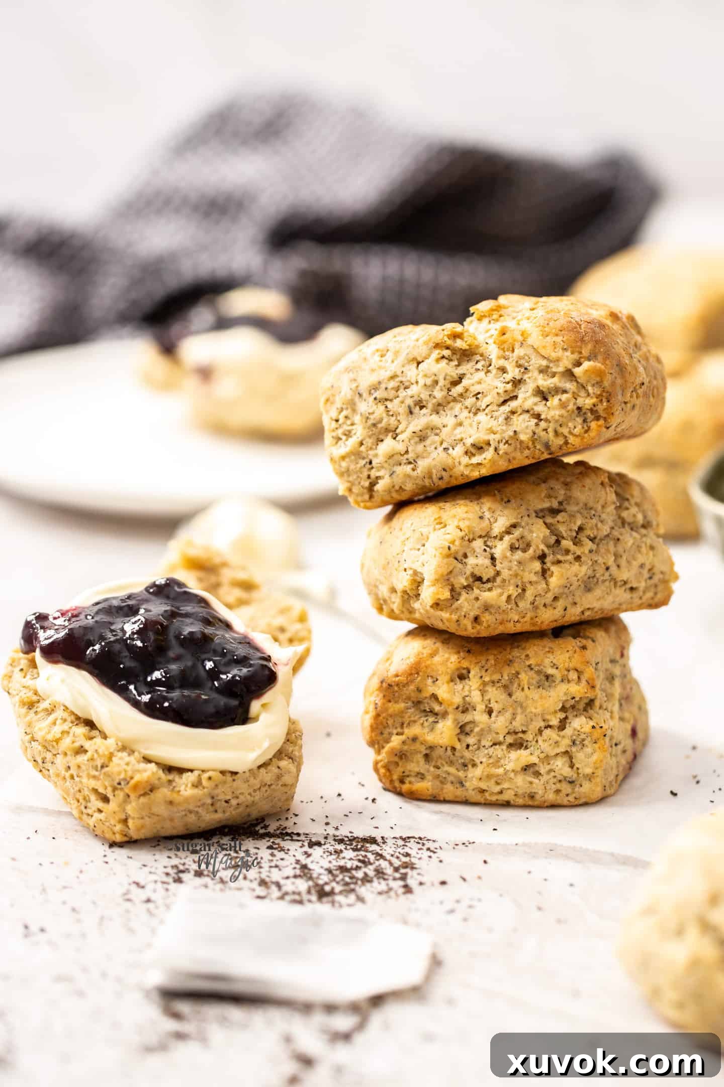 Three perfectly stacked Earl Grey scones, with a half-scone placed beside them, generously topped with clotted cream and a dollop of vibrant red jam, ready for serving.