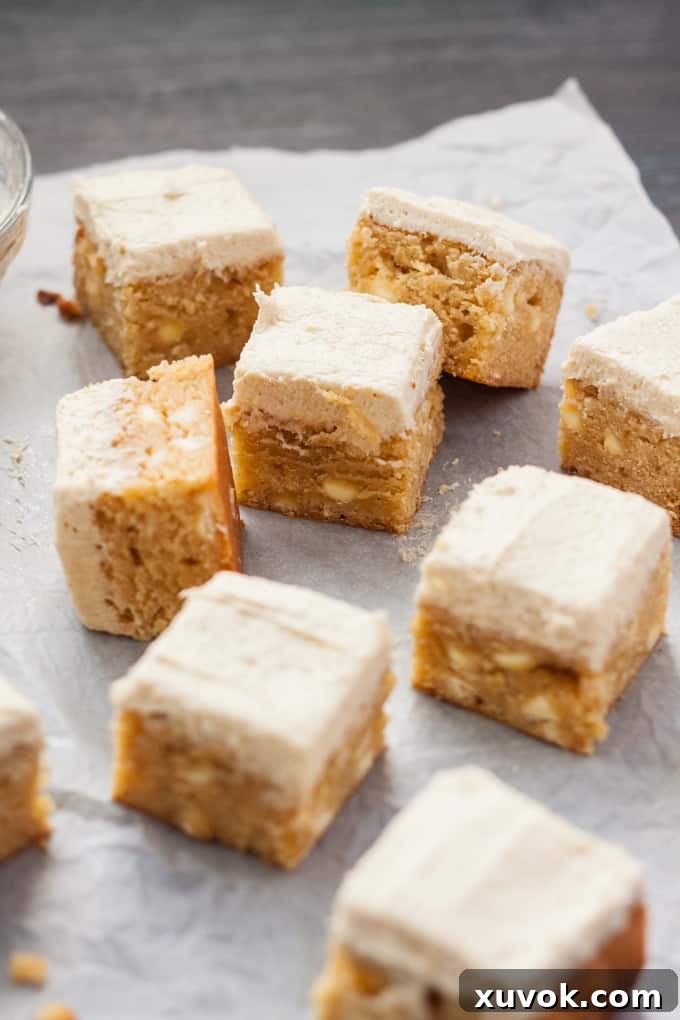 9 frosted blondies on a sheet of white baking paper.