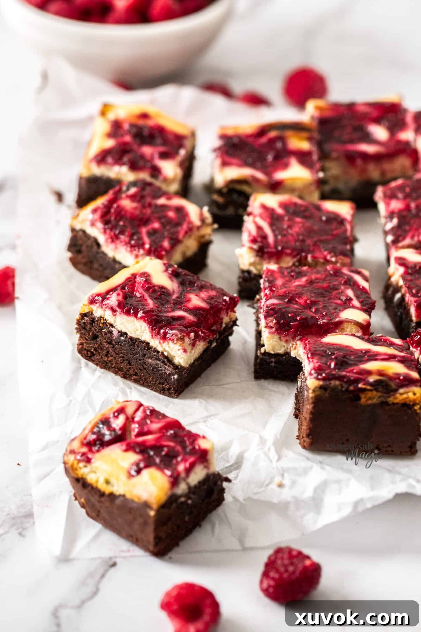 A batch of raspberry cheesecake brownies arranged artfully on a sheet of baking paper, showcasing the beautiful swirl.