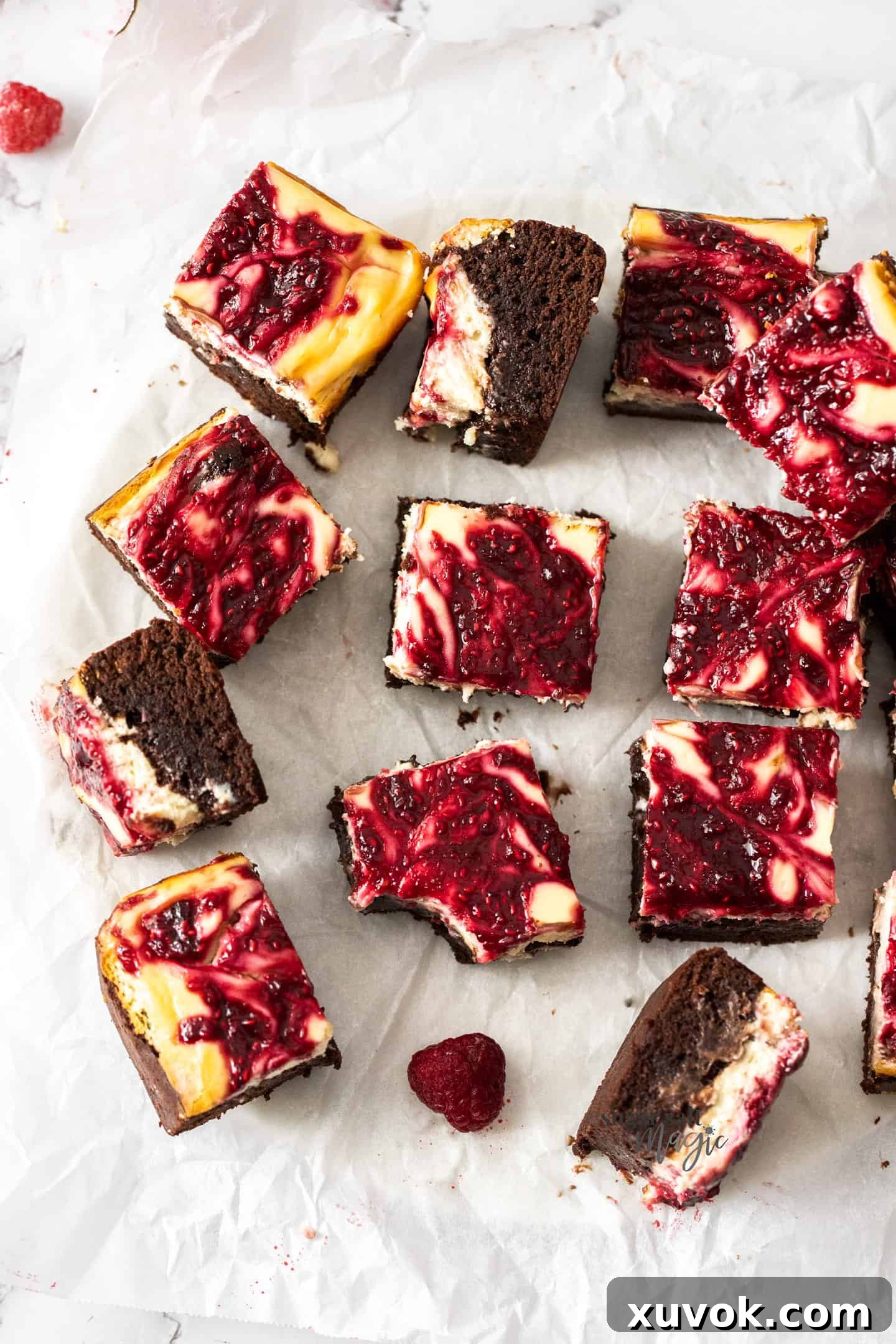A freshly baked batch of raspberry cheesecake brownies, still warm on a sheet of baking paper, ready to be sliced and enjoyed.