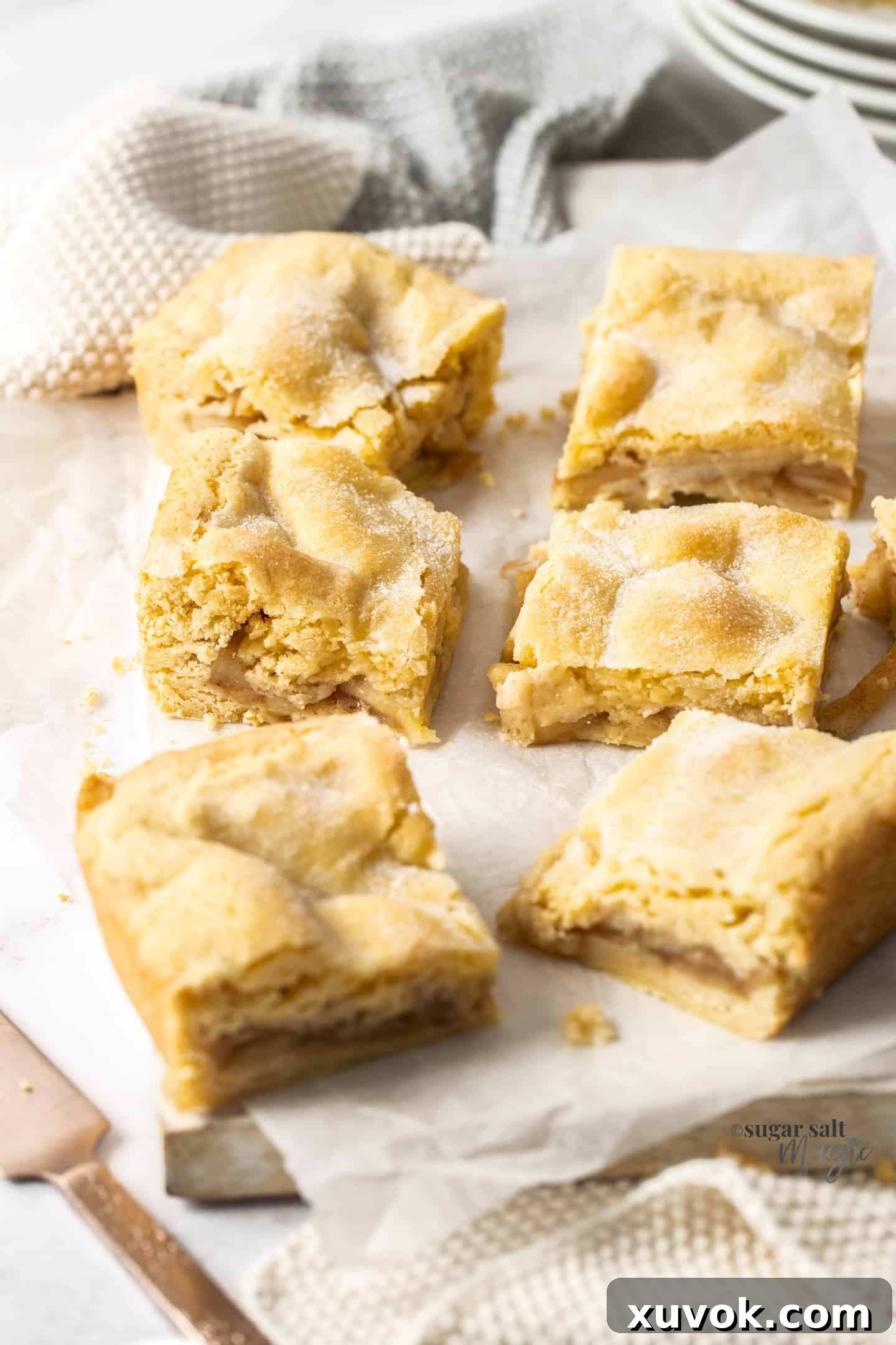 Six slices of perfectly baked apple shortcake arranged on a sheet of baking paper over a white wooden board, showcasing the golden crust and chunky apple filling.