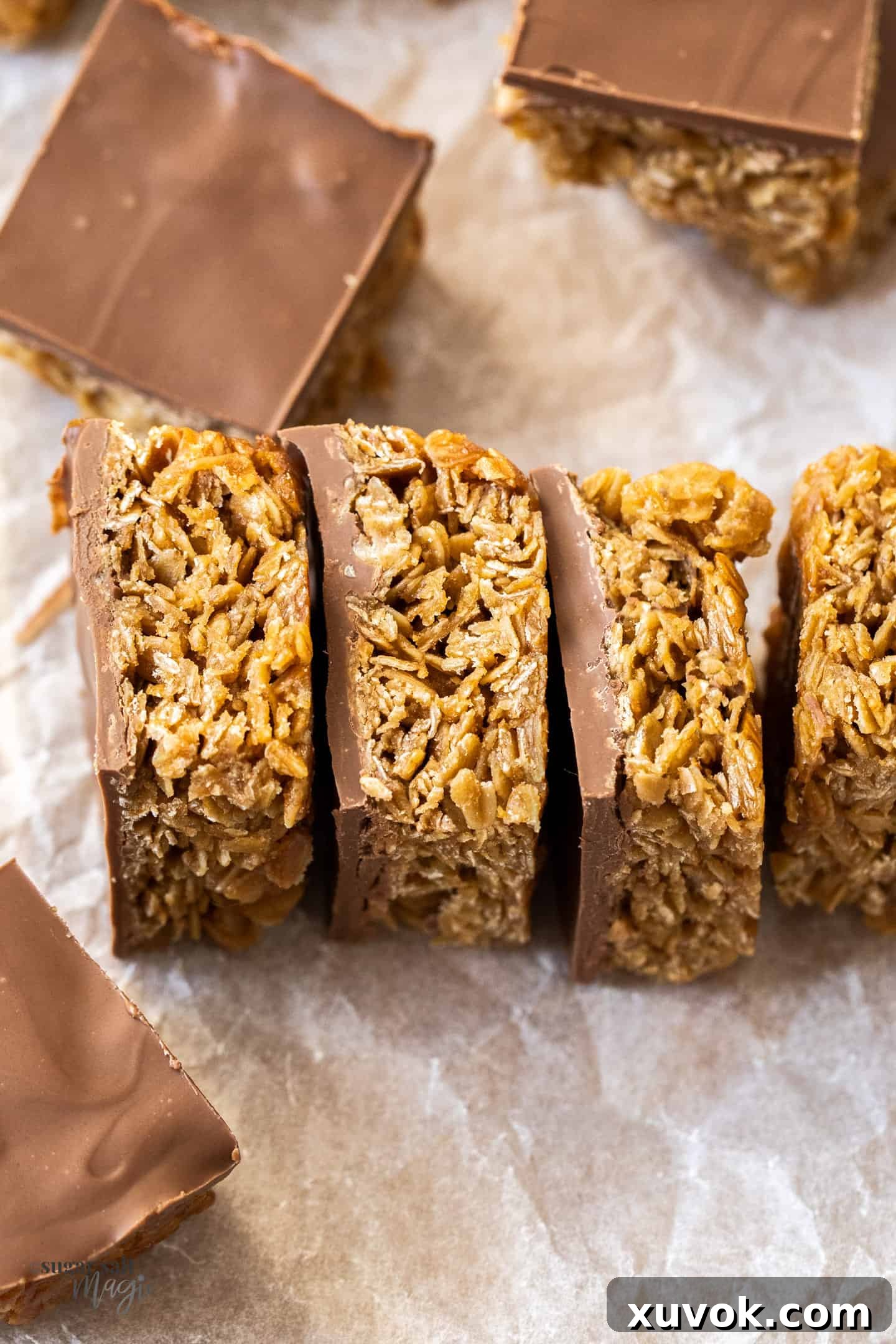 A row of perfectly cut chocolate flapjacks, neatly arranged on a sheet of baking paper, showcasing their rich chocolate topping and golden oat base.