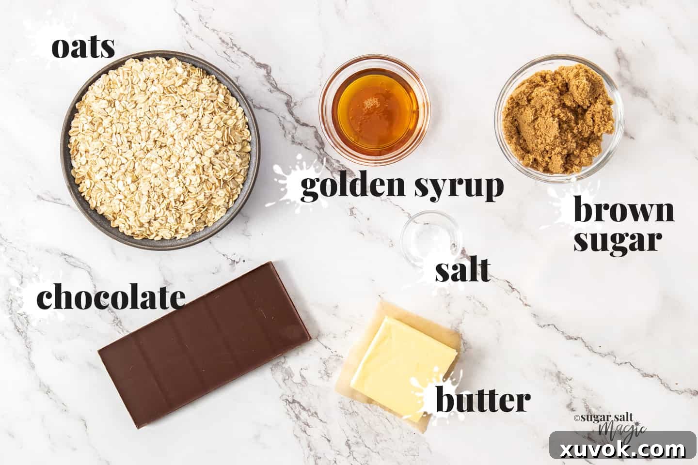 All the essential ingredients for chocolate flapjacks laid out on a pristine marble countertop, including oats, butter, golden syrup, brown sugar, salt, and milk chocolate.