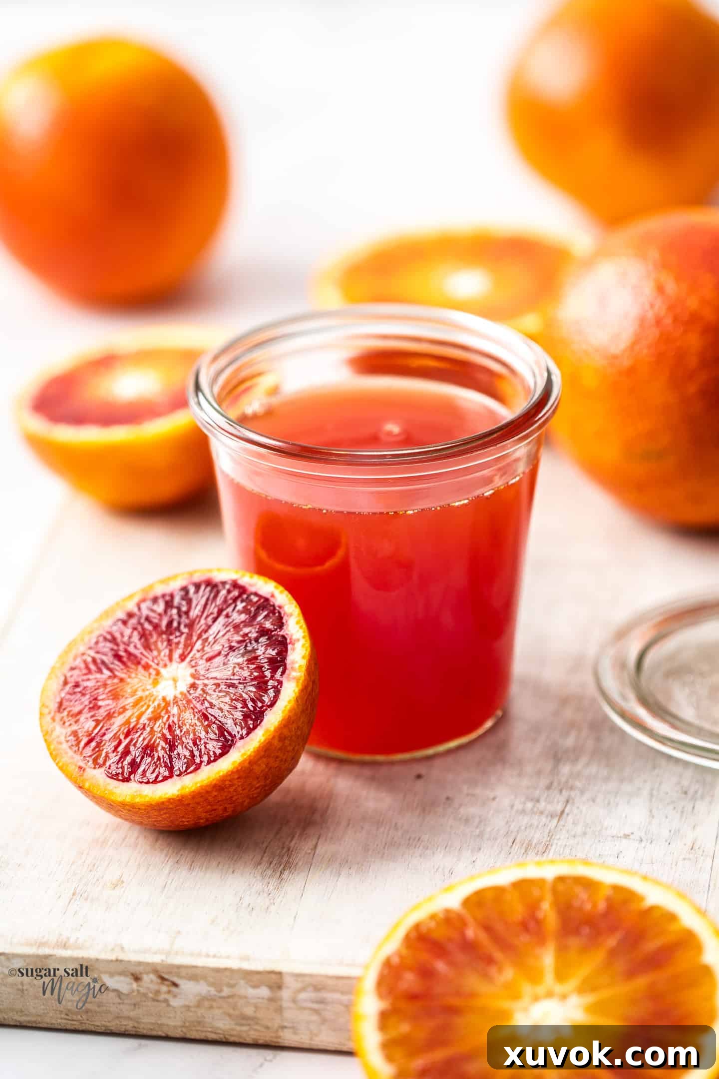 A preserving jar, filled with homemade blood orange simple syrup, elegantly surrounded by fresh oranges.