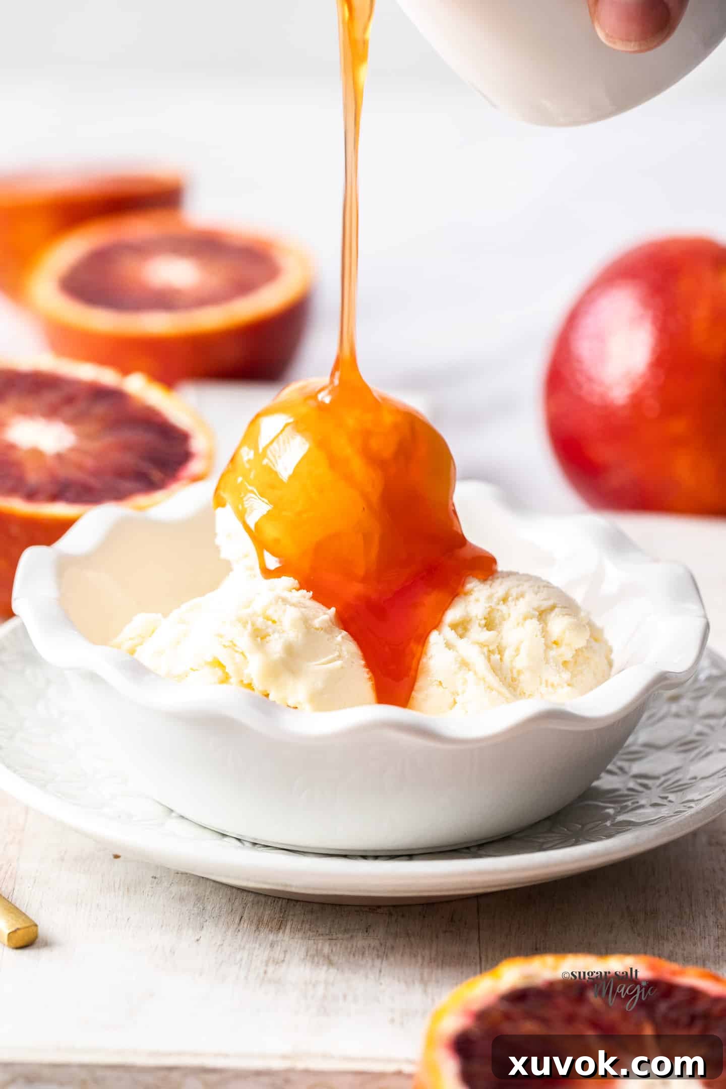 A generous pour of rich orange syrup cascades over a scoop of creamy vanilla ice cream, creating a luscious dessert.