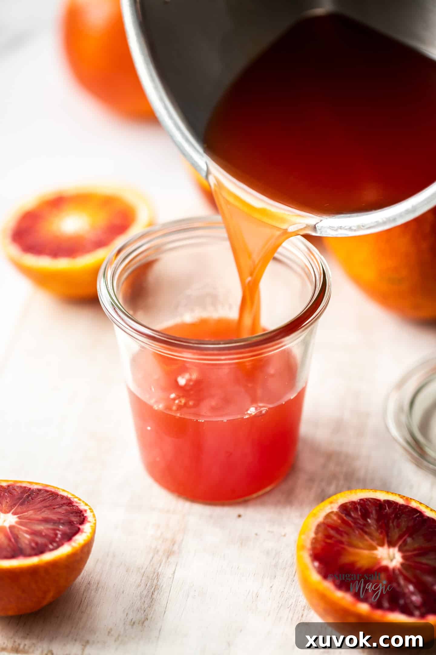 Freshly made orange simple syrup is carefully poured into a clear glass jar, ready for storage.