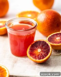 A preserving jar, filled with homemade blood orange simple syrup, elegantly surrounded by fresh oranges.