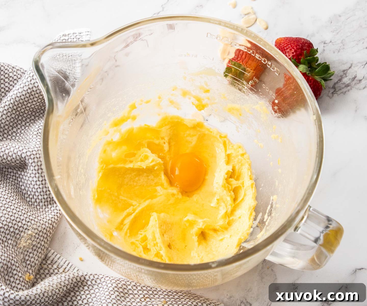 An egg being added to the creamy butter and sugar mixture in a stand mixer bowl, highlighting the light, fluffy texture.