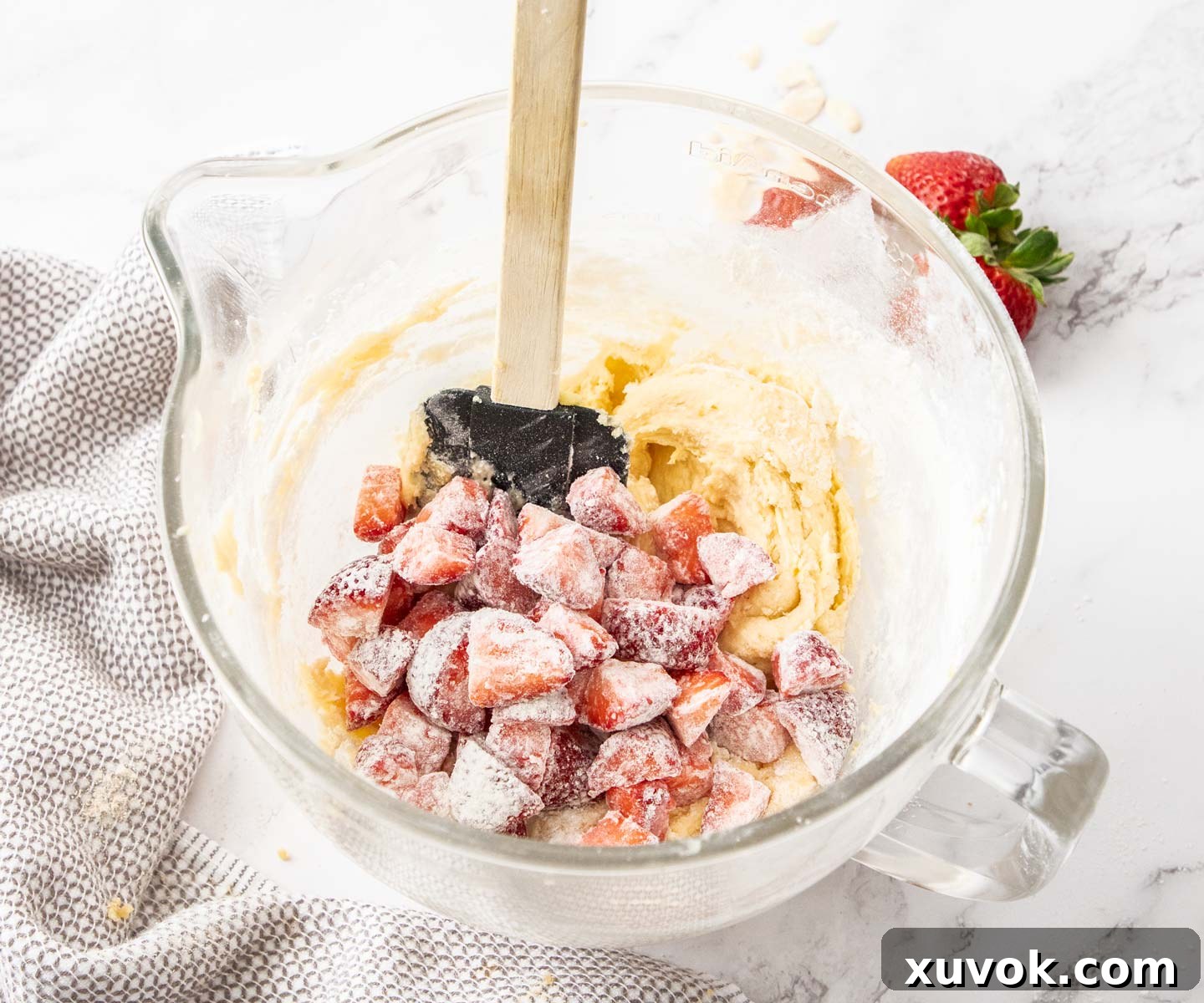 Freshly chopped strawberries, lightly coated in flour, being gently folded into the cake batter with a spatula.