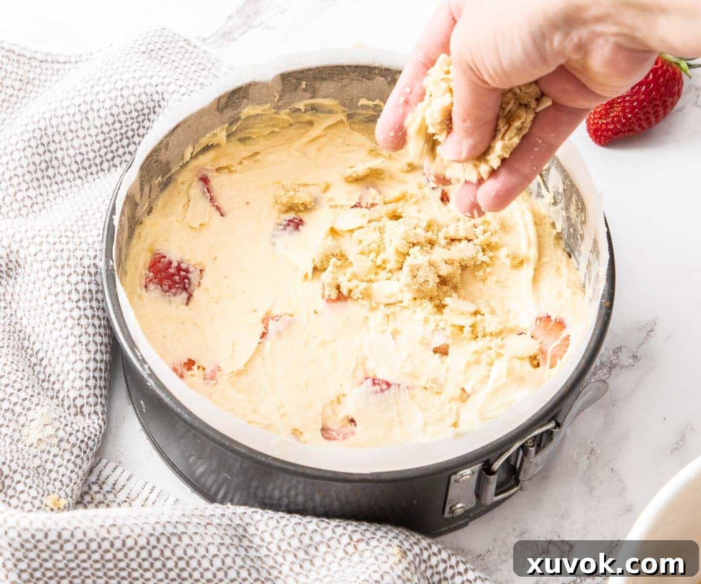 A hand sprinkling the brown sugar crumble mixture evenly over the strawberry cake batter in a springform pan before baking.